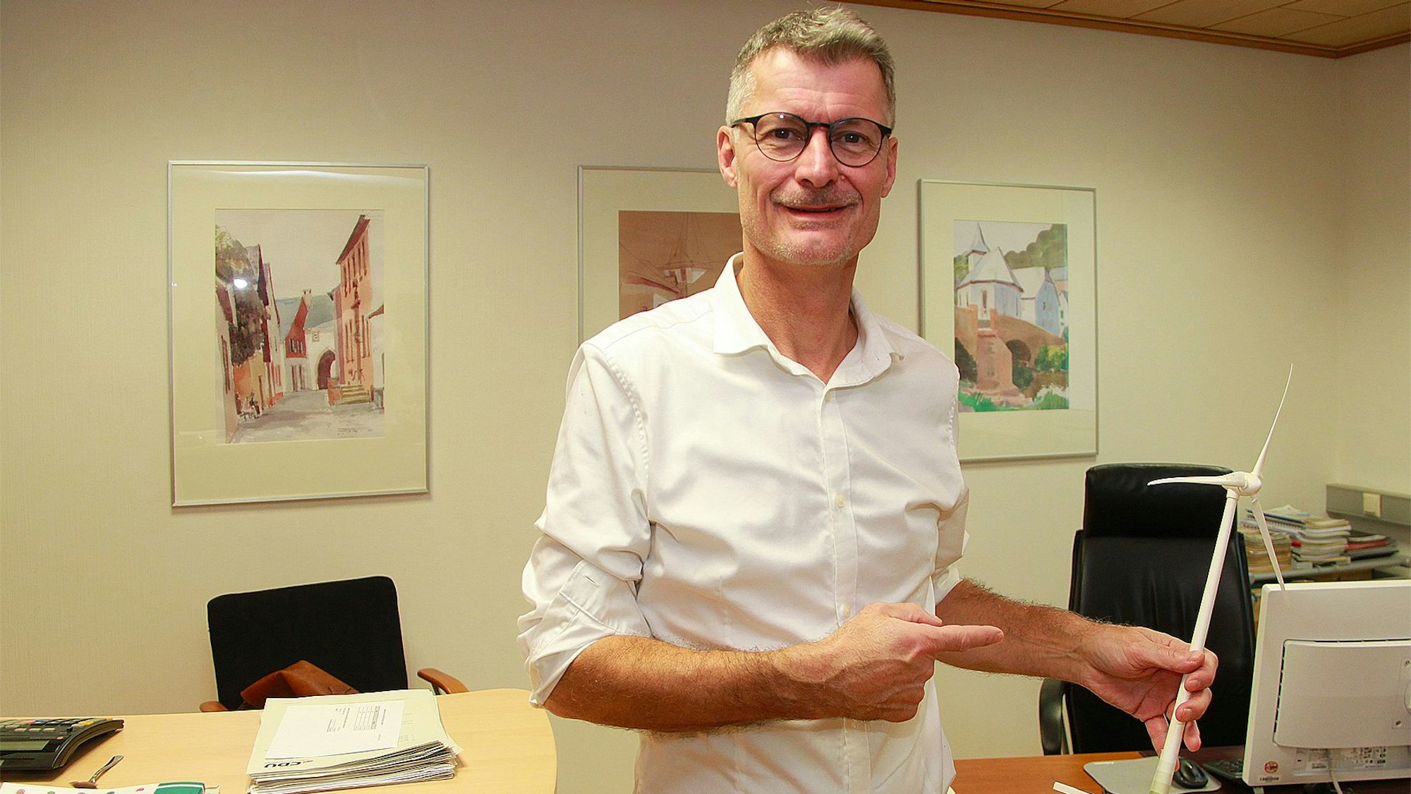Das Bild zeigt Jan Lembach in seinem Büro. Er hält das Modell einer Windkraftanlage in der Hand.
