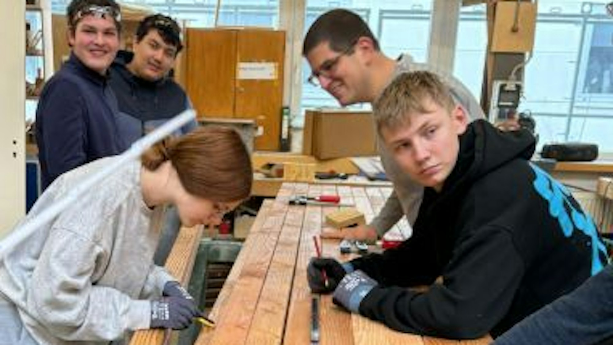 Vier Jugendliche und ein Erwachsener arbeiten mit Holzlatten.
