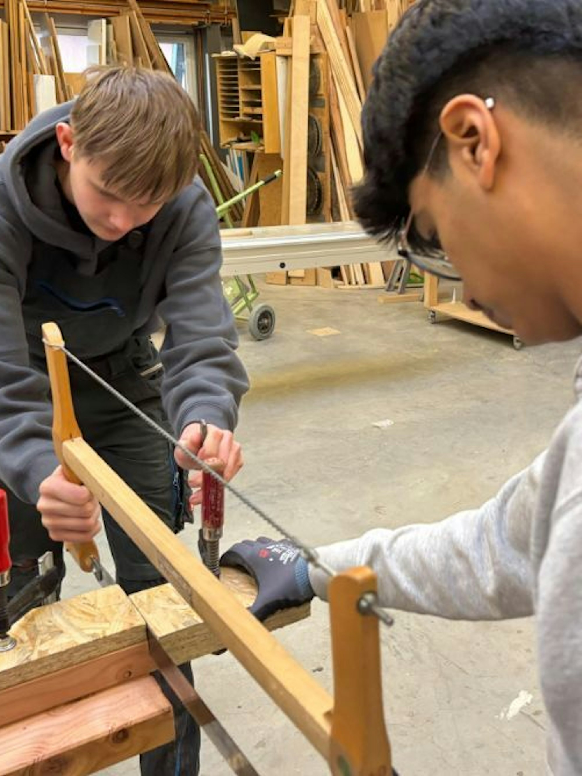 Zwei Jugendliche sägen mit einer Säge Holz.