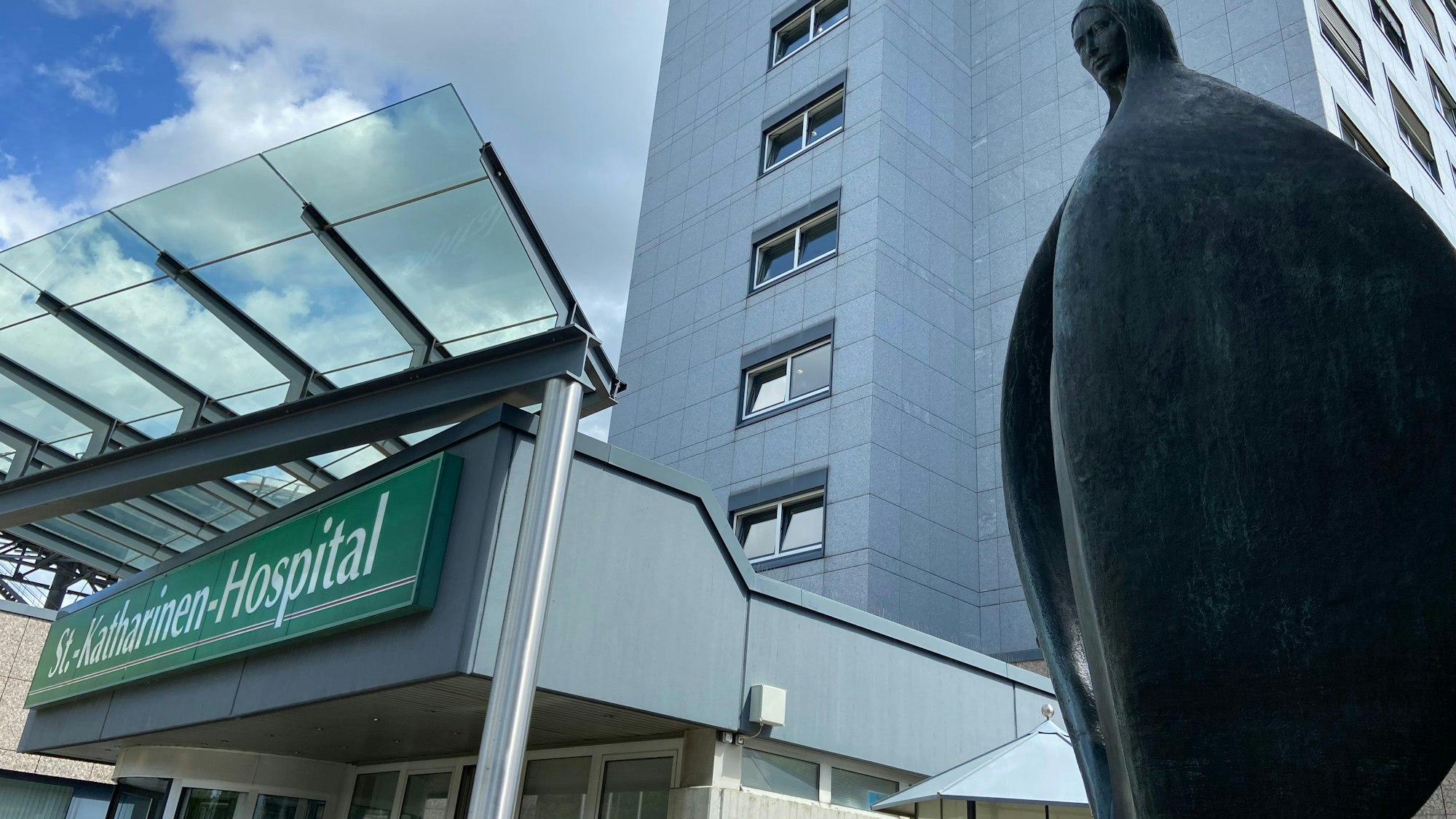 Auf dem Bild ist das Gebäude des Krankenhauses und eine Skulptur zu sehen.