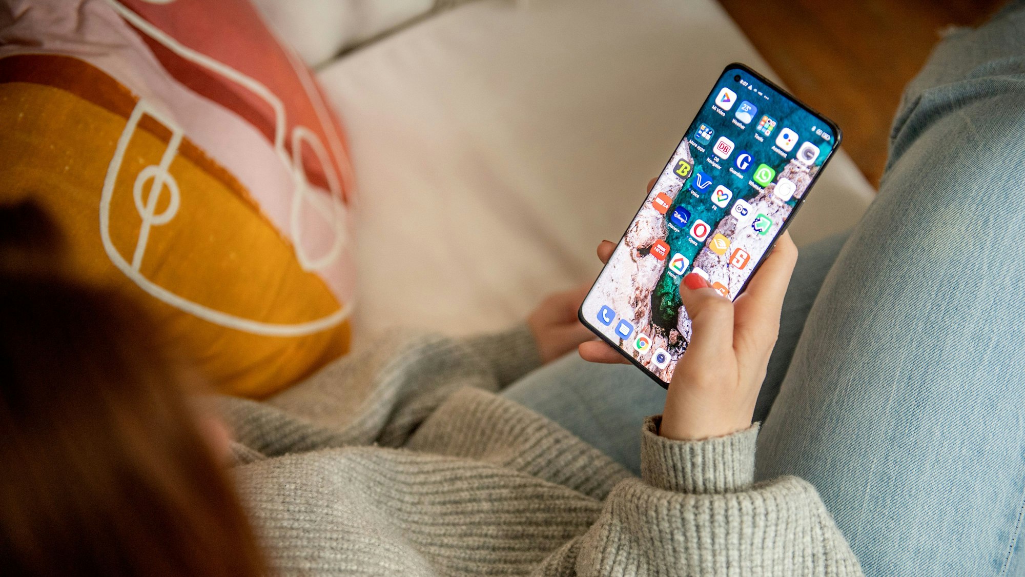 Eine Frau sitzt auf dem Sofa und schaut auf ihr Smartphone.