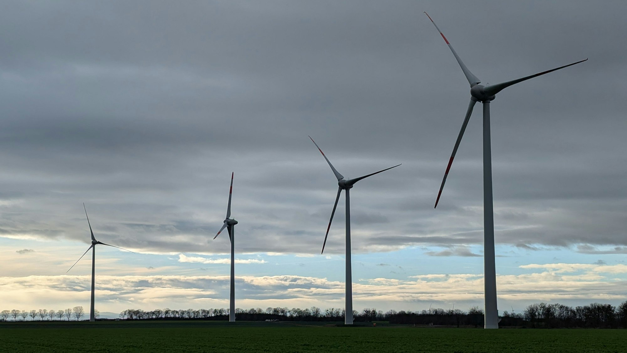 Windkraftanlagen sind vor einem bewölkten Himmel in Hürth zu sehen.