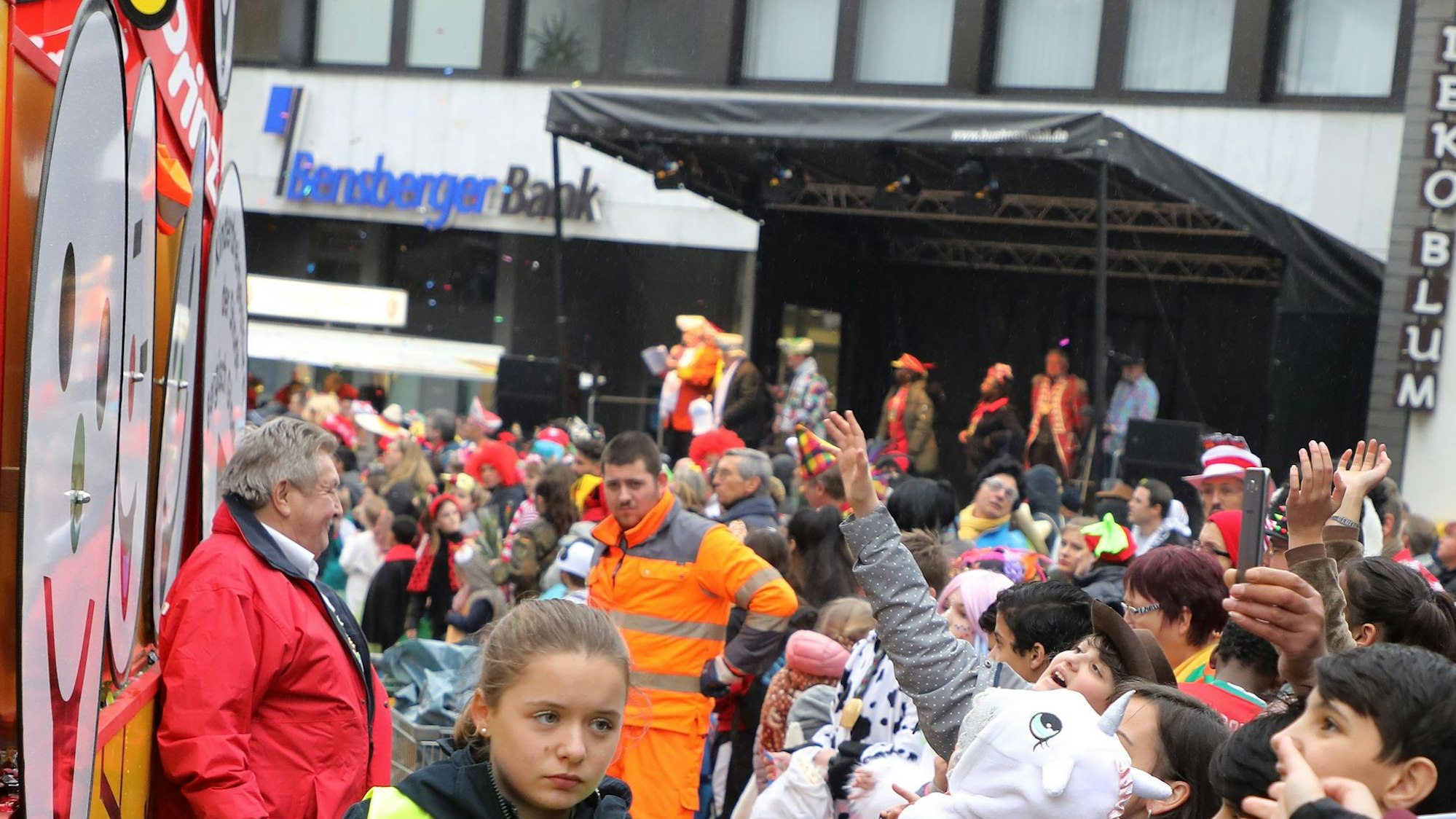 Menschen stehen am Bensberger Zugweg, im Hintergrund ist die Bühne an der Bensberger Bank zu sehen.