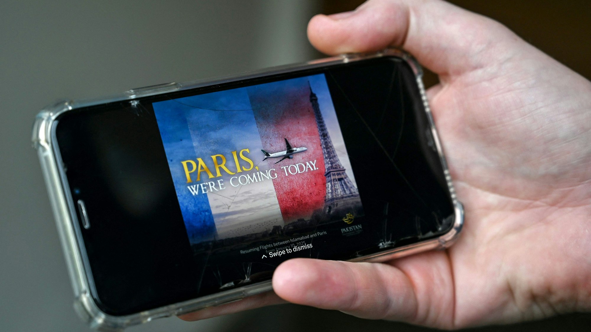 Ein Mann schaut sich auf seinem Mobiltelefon in Islamabad eine Werbung des Flugzeugs der Pakistan International Airlines (PIA) an, das auf den Eiffelturm zufliegt.