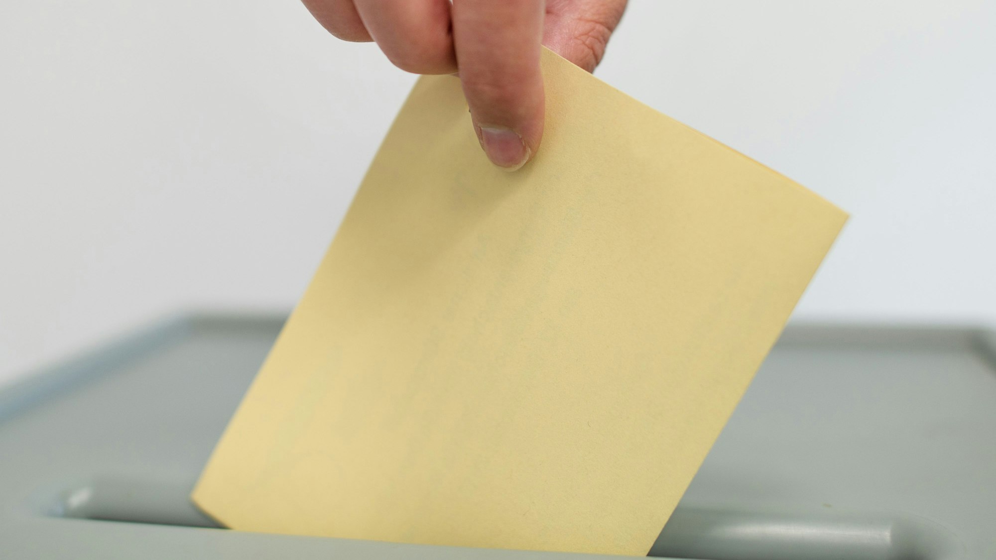 Eine Hand wirft einen Wahlzettel in eine Box.