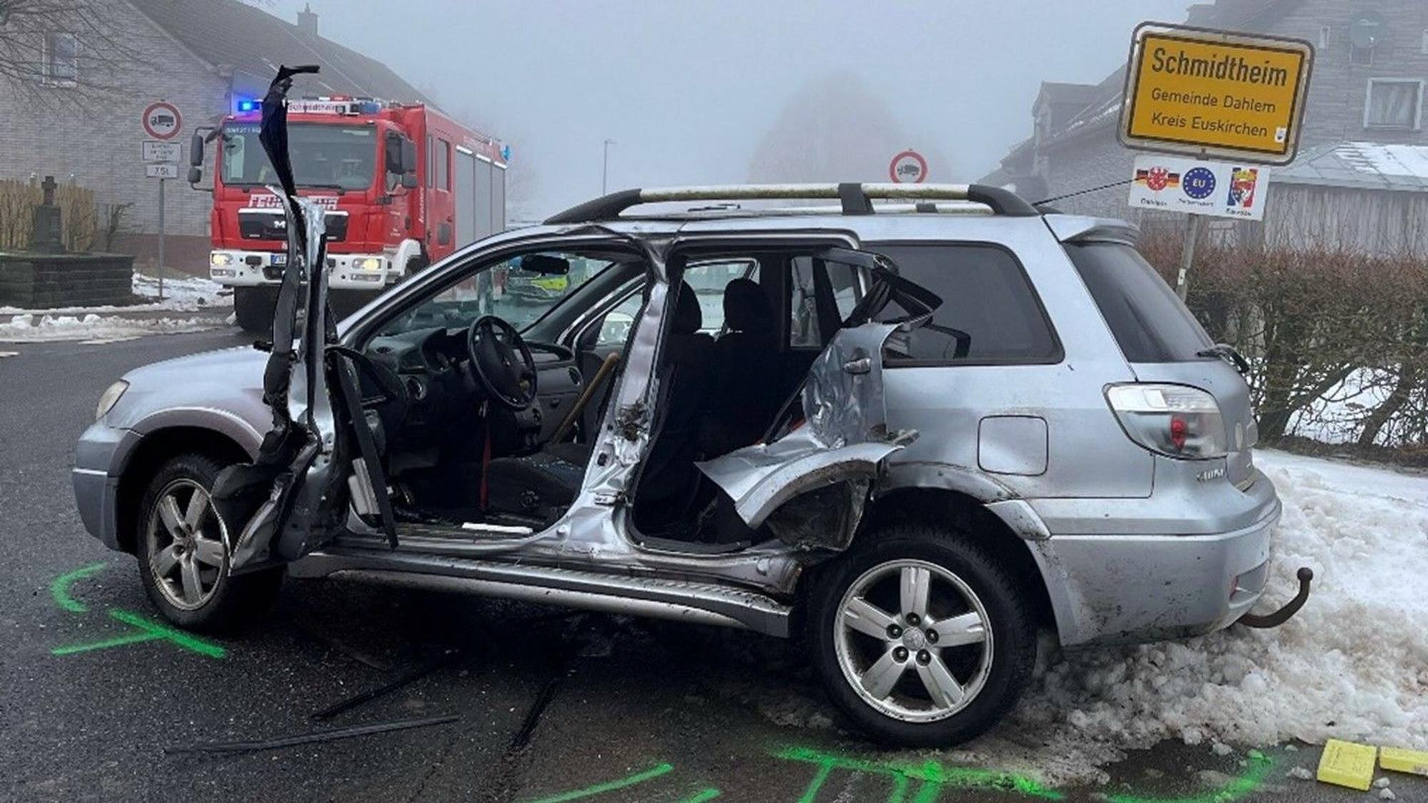 Ein silberfarbenes Auto steht nach einem Unfall massiv beschädigt auf einer Straße. Rechts dahinter ist das Ortsschild von Schmidtheim zu sehen, links ein Feuerwehrfahrzeug.
