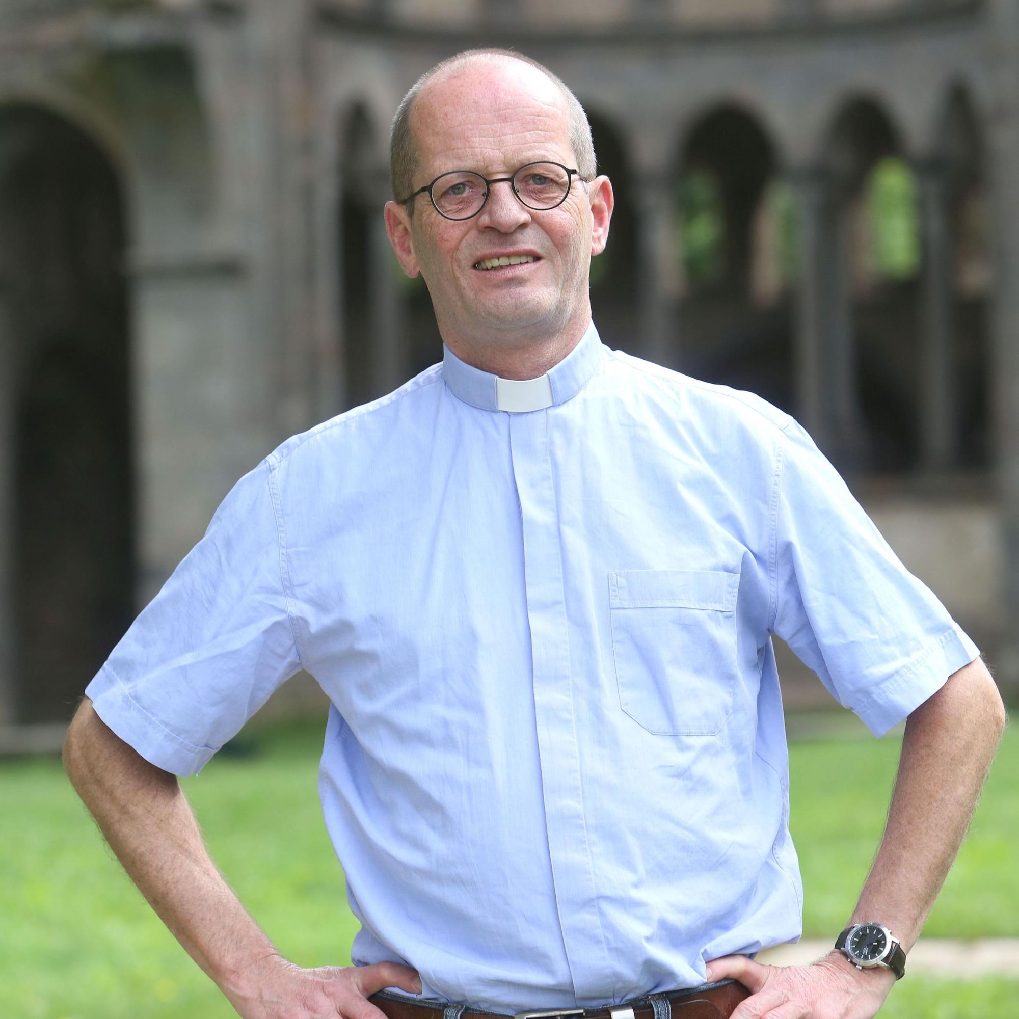Ein Priester im blauen Hemd vor der Chorruine von Heisterbach.