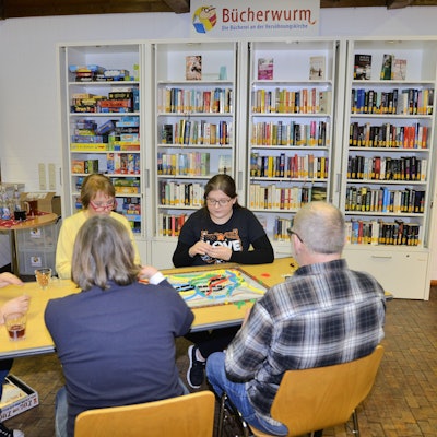 Fünf Personen sitzen um einen Tisch und spielen Gesellschaftsspiele.