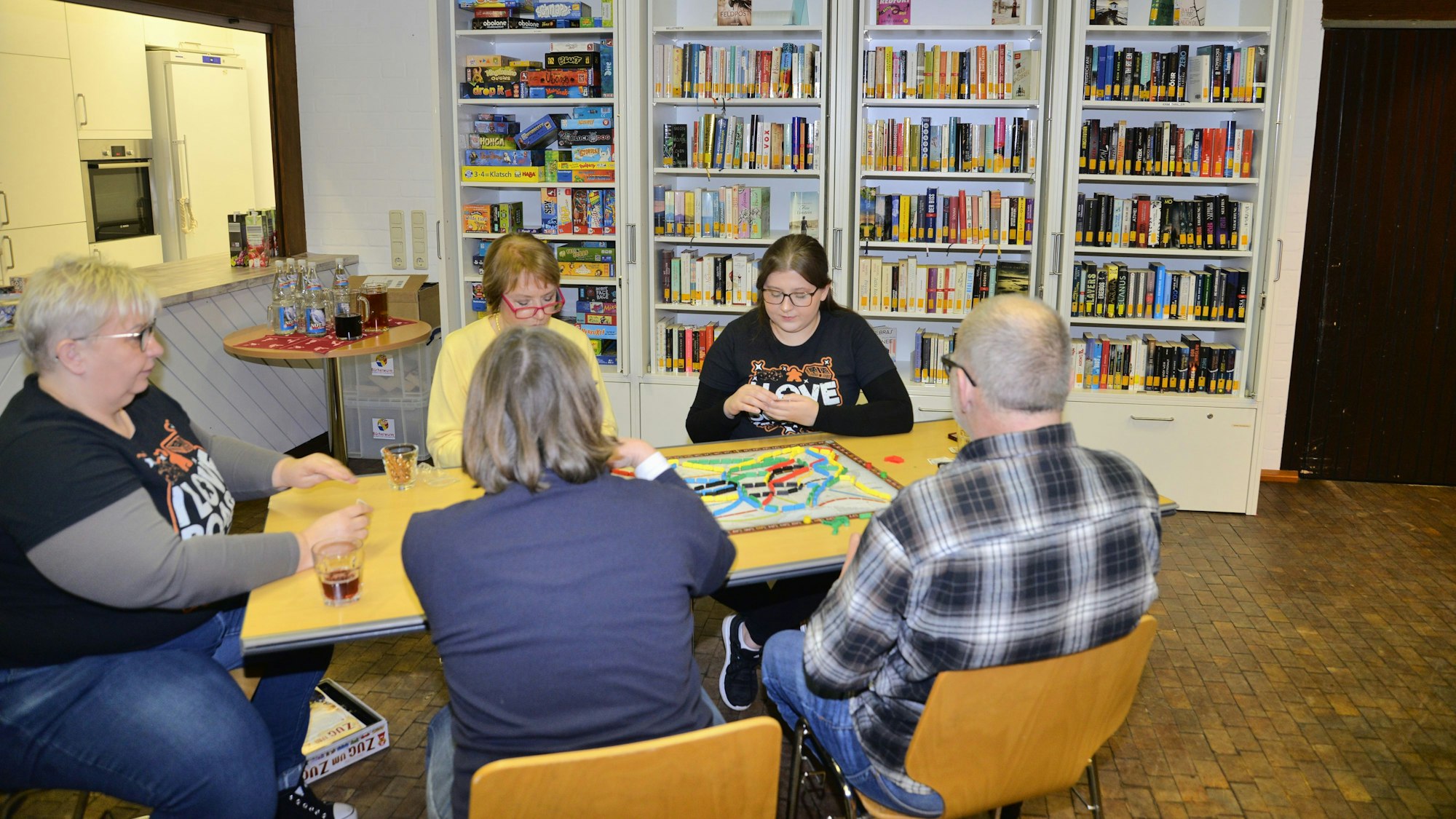 Fünf Personen sitzen um einen Tisch und spielen Gesellschaftsspiele.