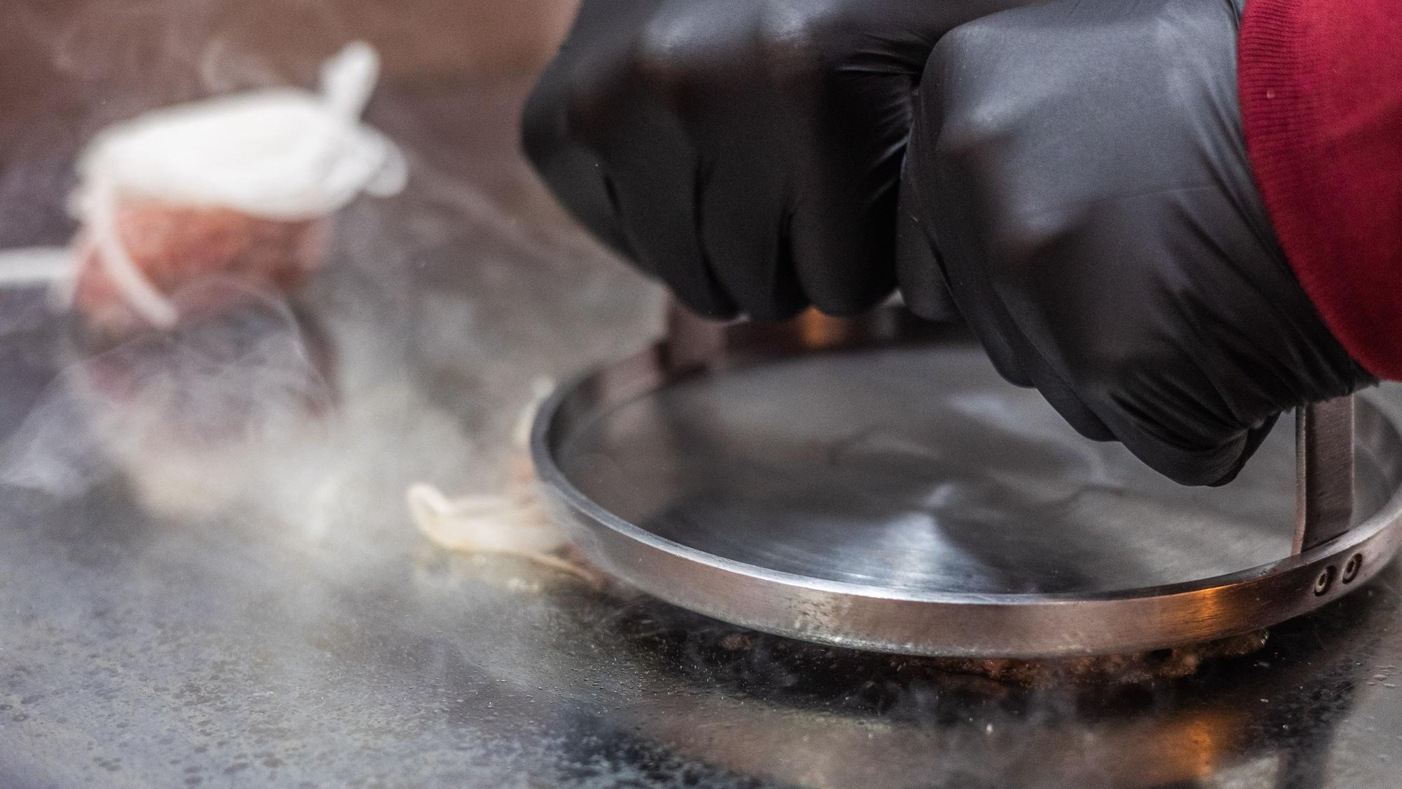 Auf der Grillplatte wird das Fleisch platt gedrückt.