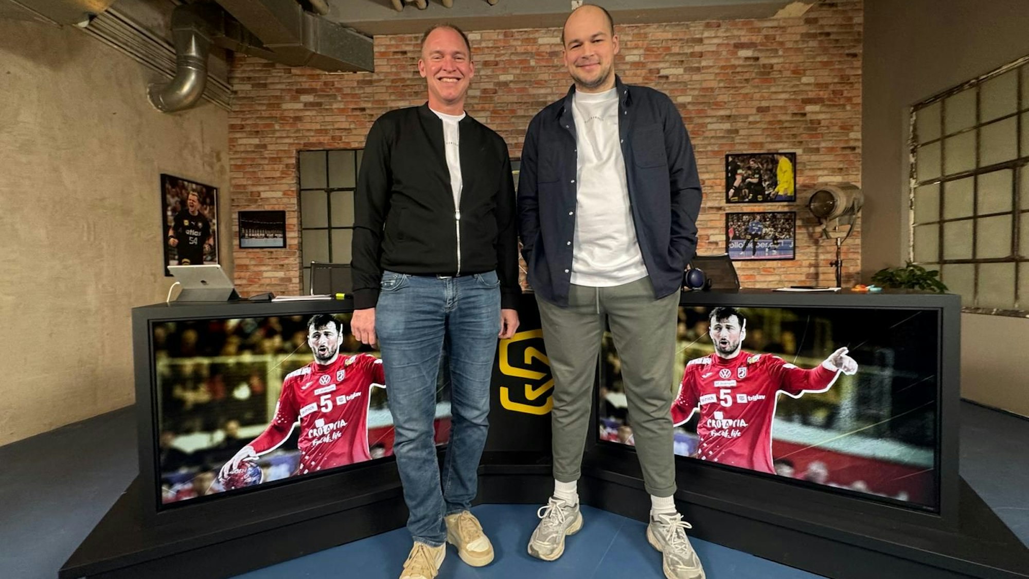 Paul Drux und Maik Thiele stehen vor großen Bildschirmen, auf denen sich die Kroaten auf ihr Spiel vorbereiten.