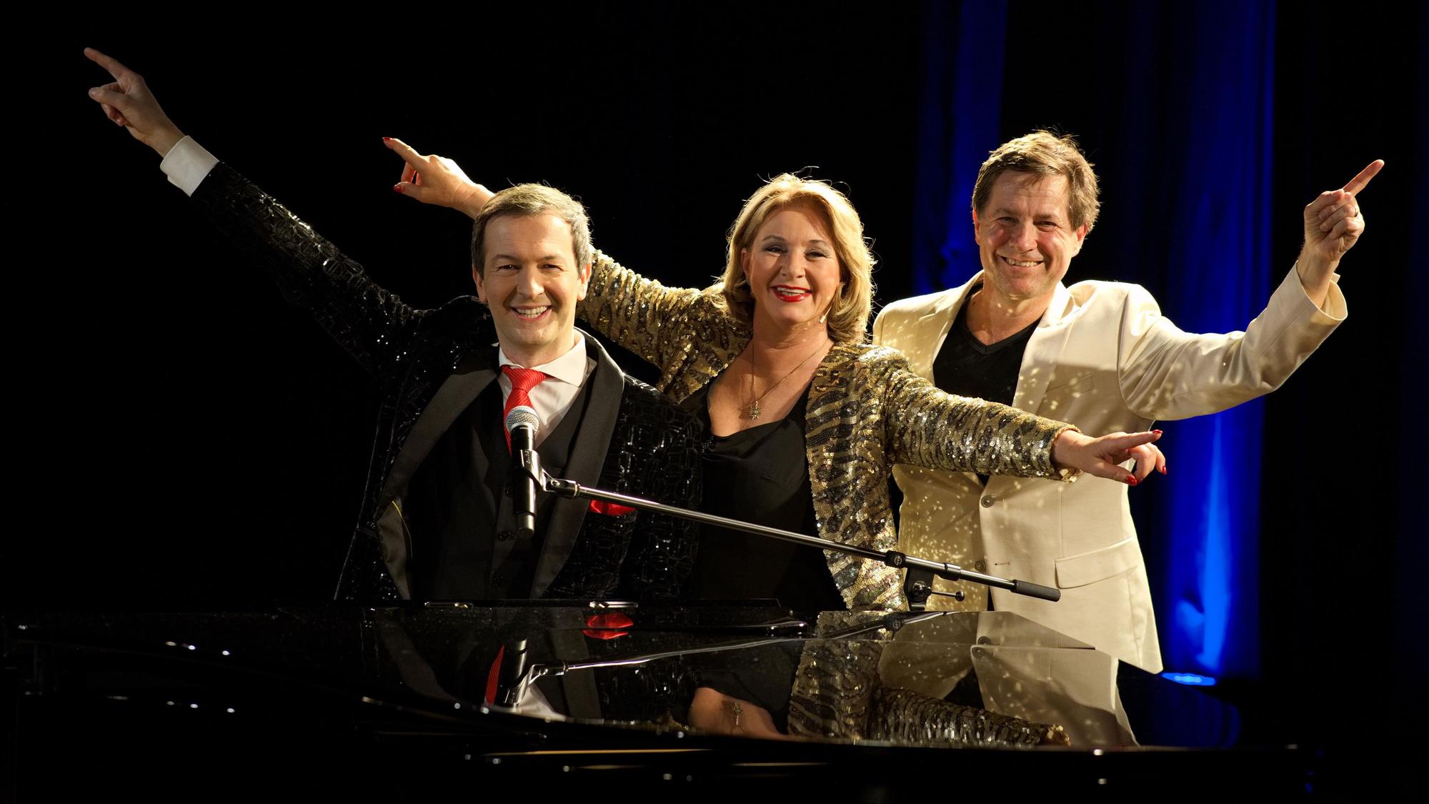 Alex Parker (v.l.), Gabriela Benesch und Erich Furrer stehen nebeneinander und recken die Arme zur Seite.