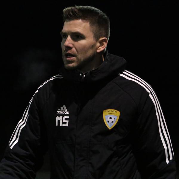 Der Trainer der A-Jugend der JSG Erft 01 Euskirchen, Marcel Schmitz, trägt eine dicke Jacke mit Initialien und Vereinslogo.