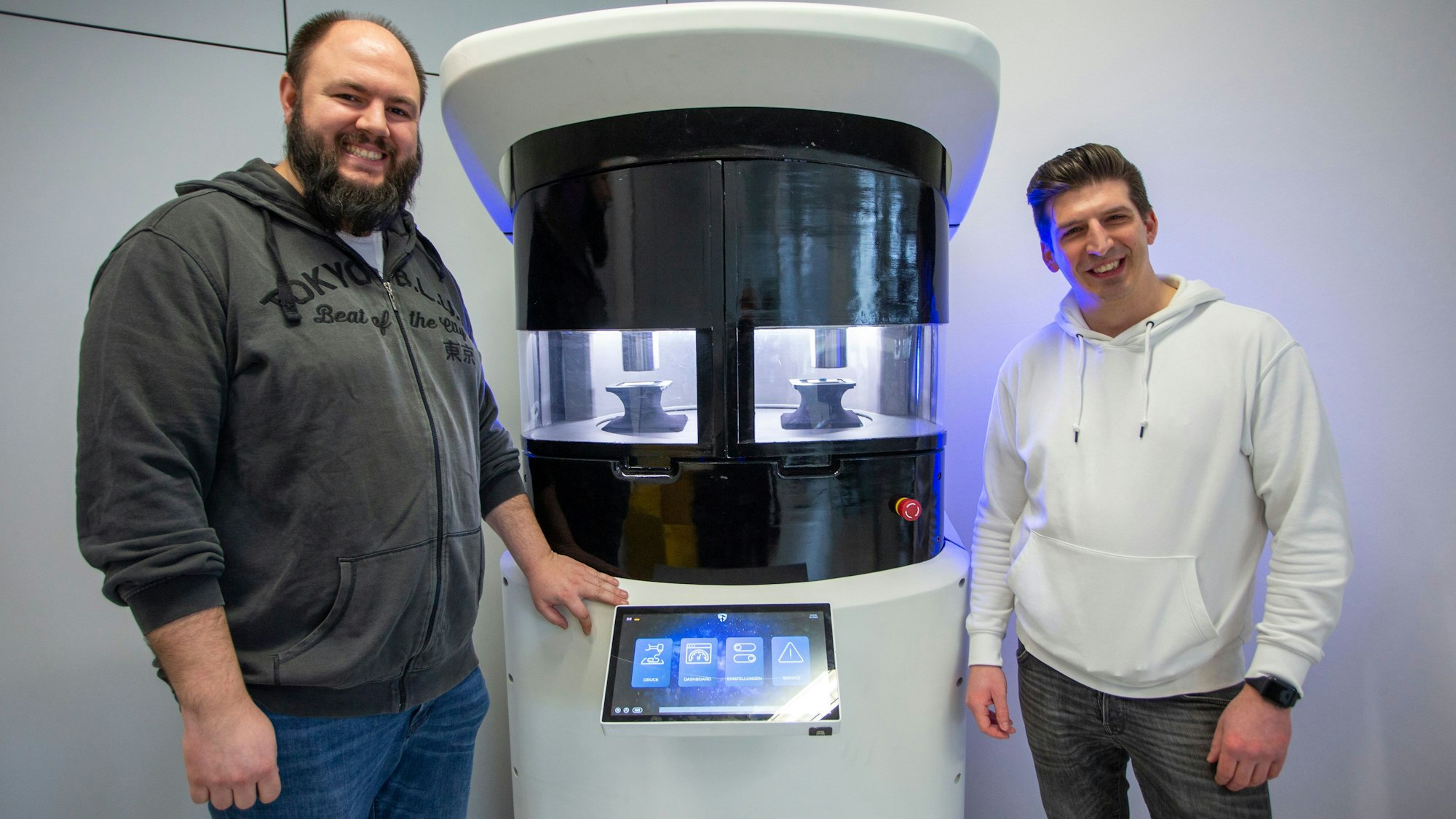 Zwei junge Männer stehen neben einer Maschine.