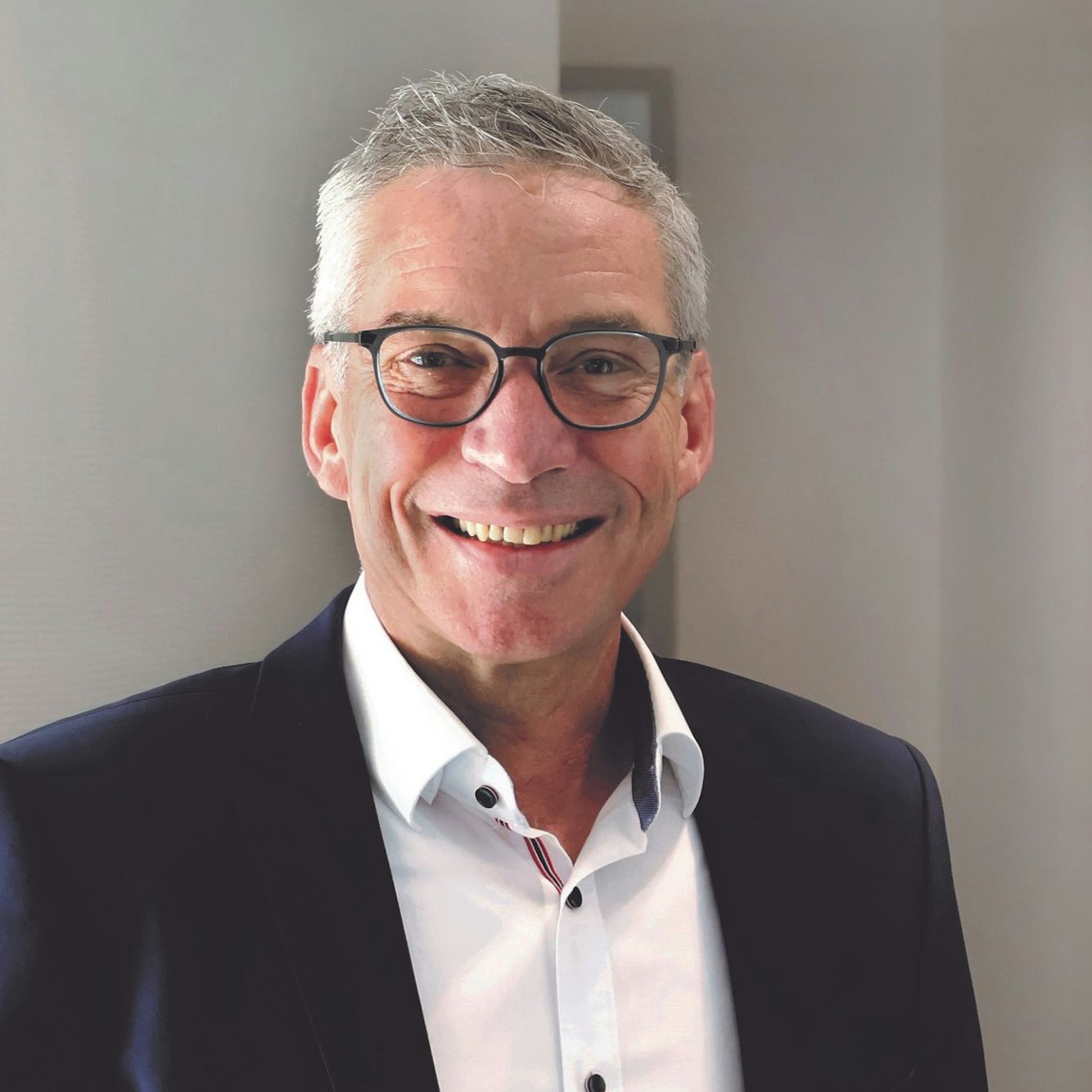 Wolfgang Schneider blickt lächelnd in die Kamera. Er trägt ein weißes Hemd und ein dunkles Sakko.