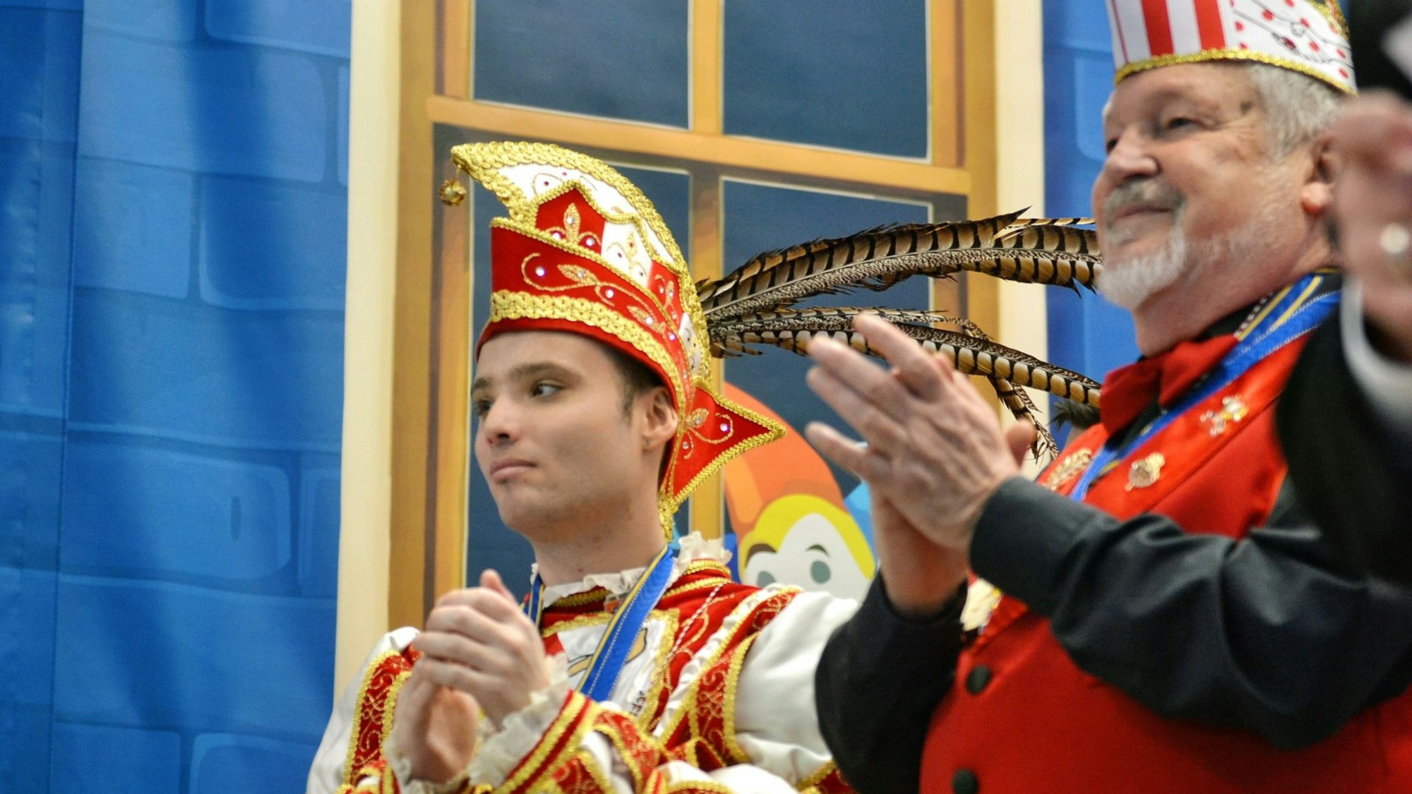 Der junge Prinz applaudiert auf der Bühne zusammen mit einem anderen Karnevalisten nach einer Darbietung.