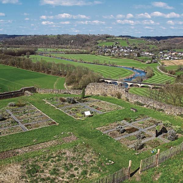 Blick über Gartenbeete mit Bruchsteinmauer in ein Tal.