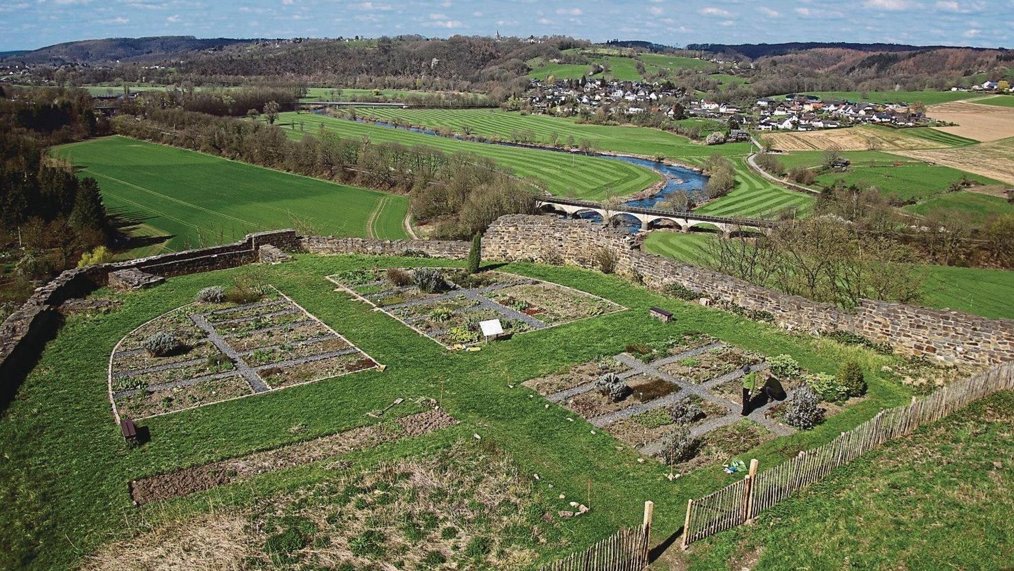 Blick über Gartenbeete mit Bruchsteinmauer in ein Tal.