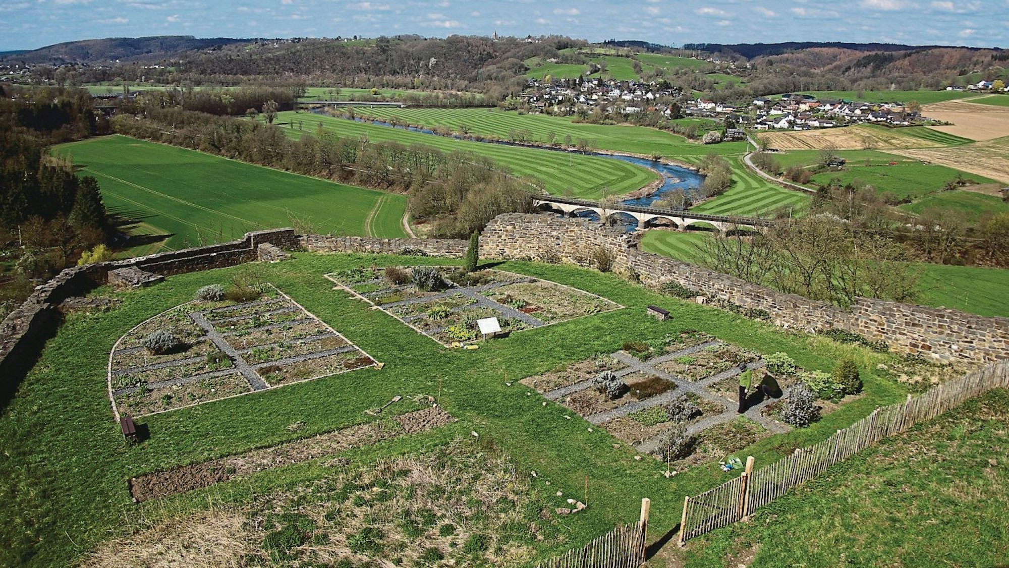 Blick über Gartenbeete mit Bruchsteinmauer in ein Tal.