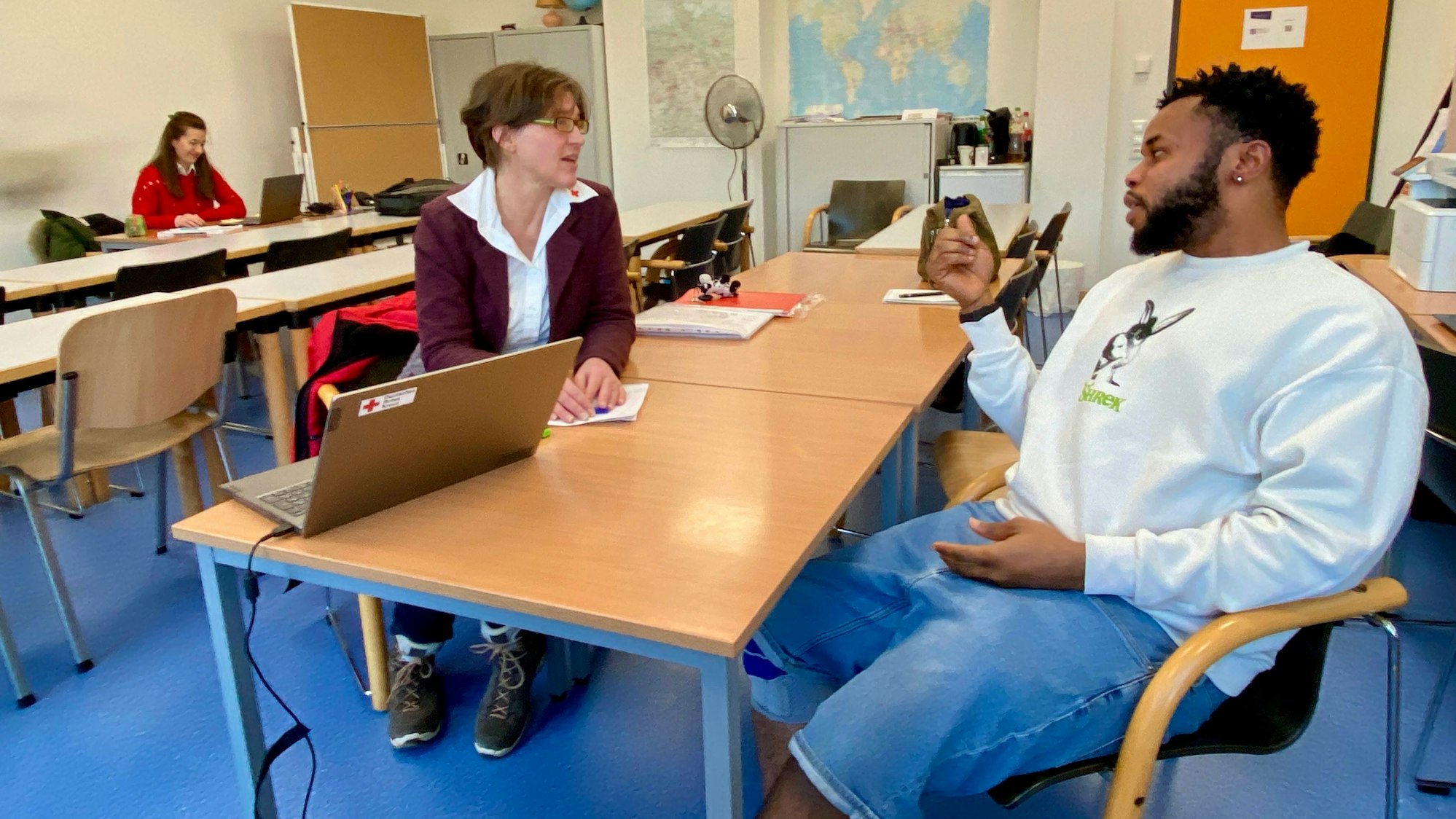 Ein Mann und eine Frau sitzen sich in der Flüchtlingsunterkunft Weilerswist an einem Tisch gegenüber und unterhalten sich.