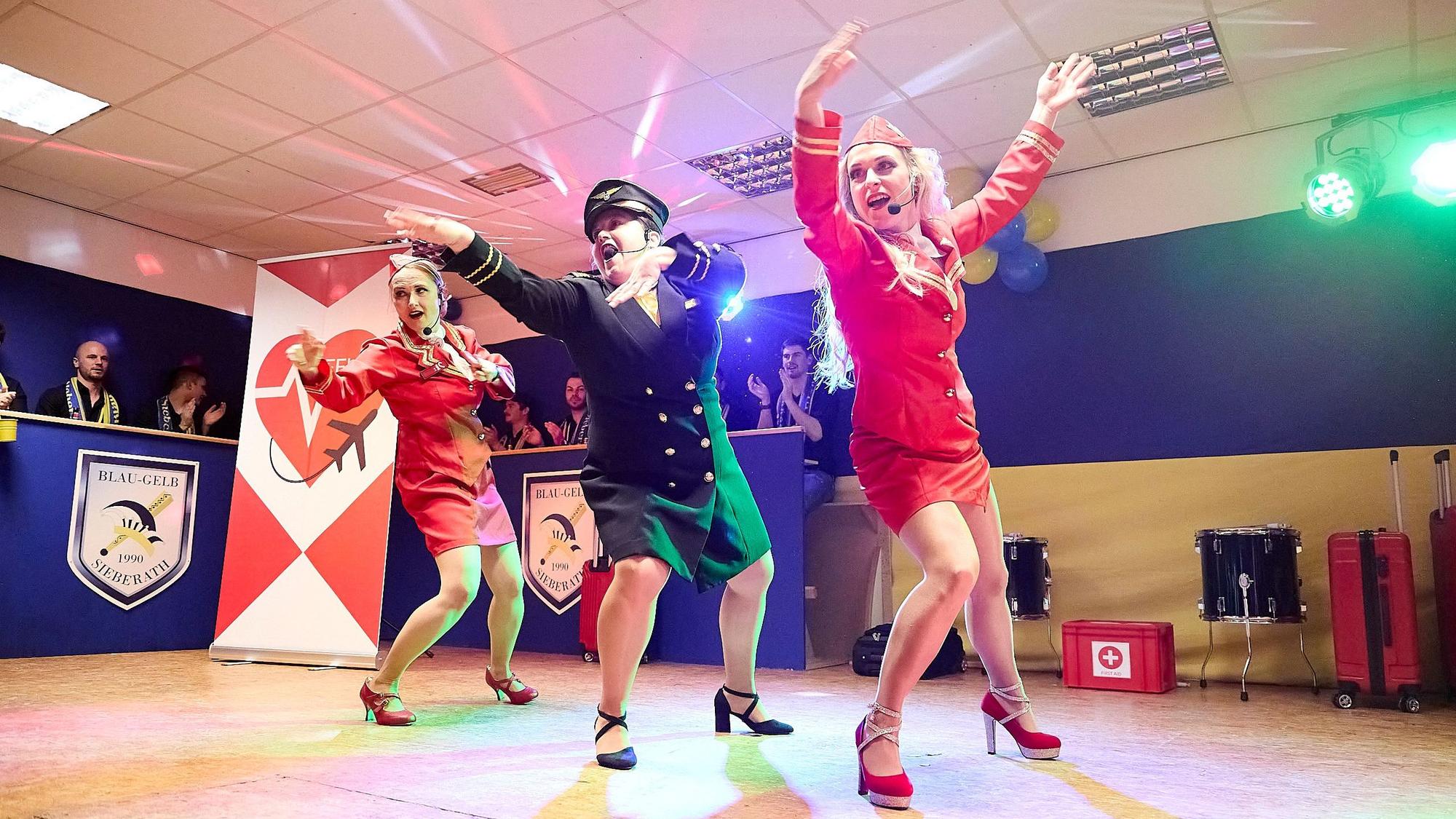 Drei Frauen tragen Flugbegleiterinnen-Kostüme und tanzen im Karneval auf der Bühne in Hellenthal-Wolfert.