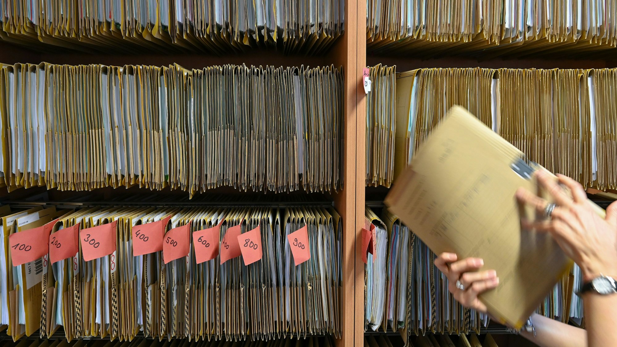 Eine Mitarbeiterin greift an einem Regal nach einer Akte.