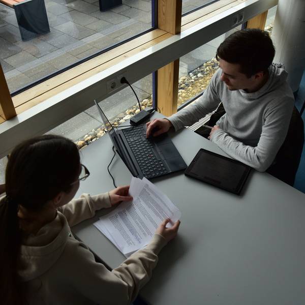 Junge Leute sitzen an einem Tisch und arbeiten am Laptop.