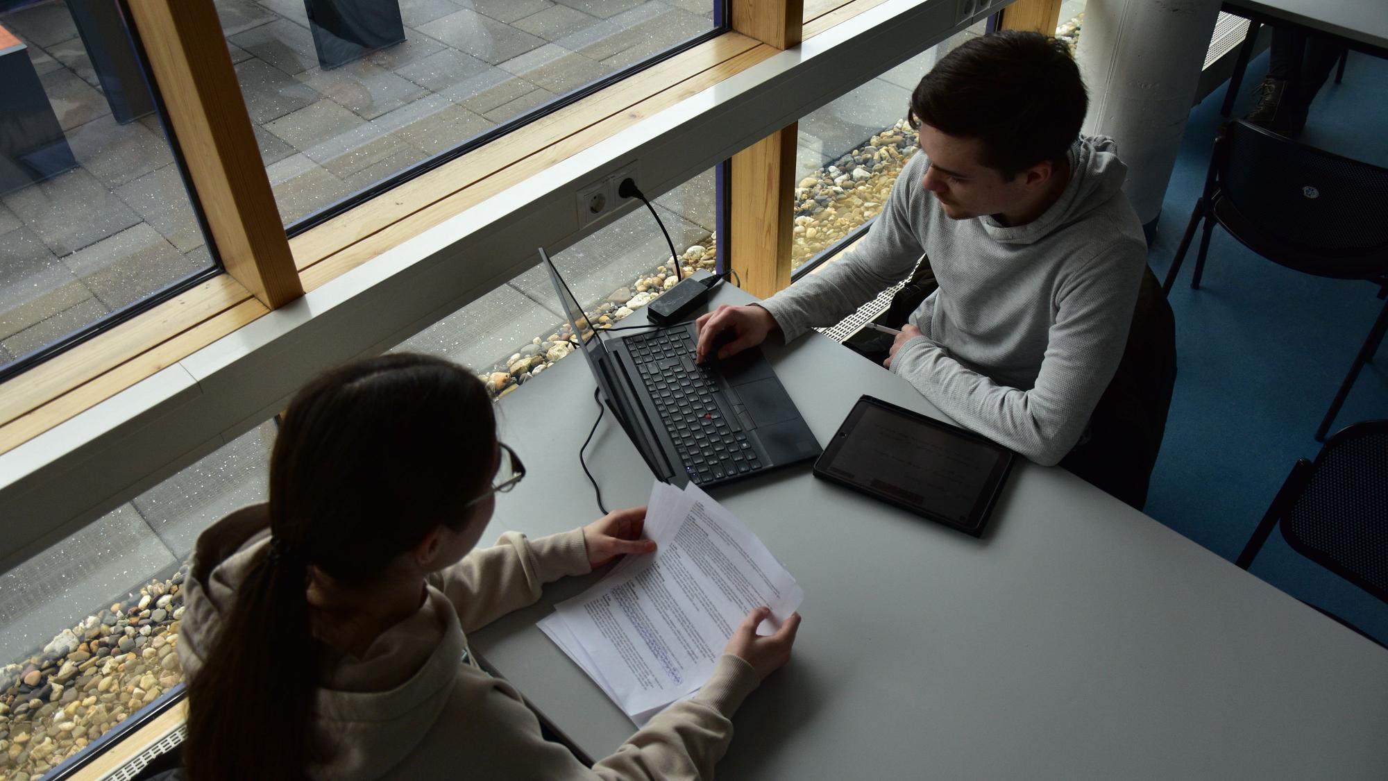 Junge Leute sitzen an einem Tisch und arbeiten am Laptop.