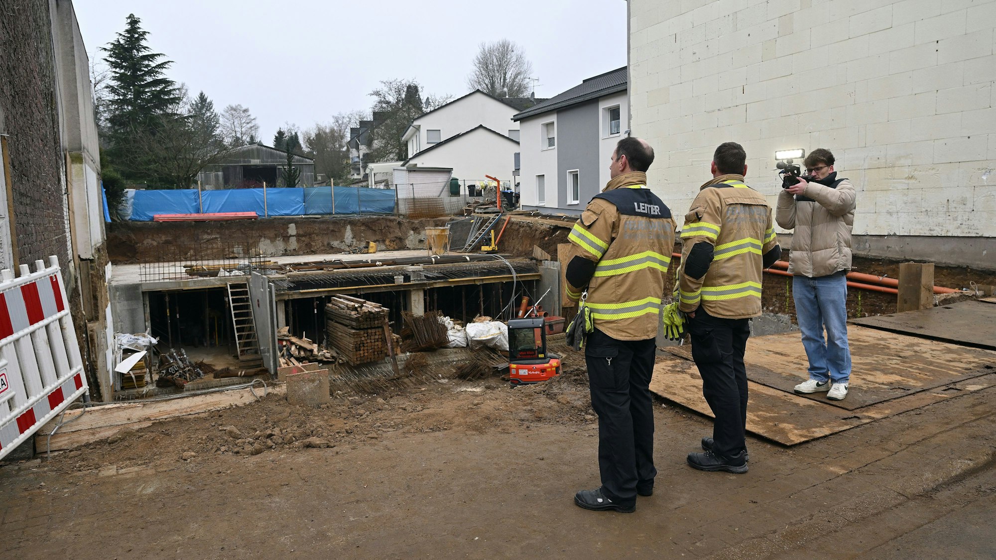 Von hinten sieht man drei Männer, die in die Baugrube blicken.