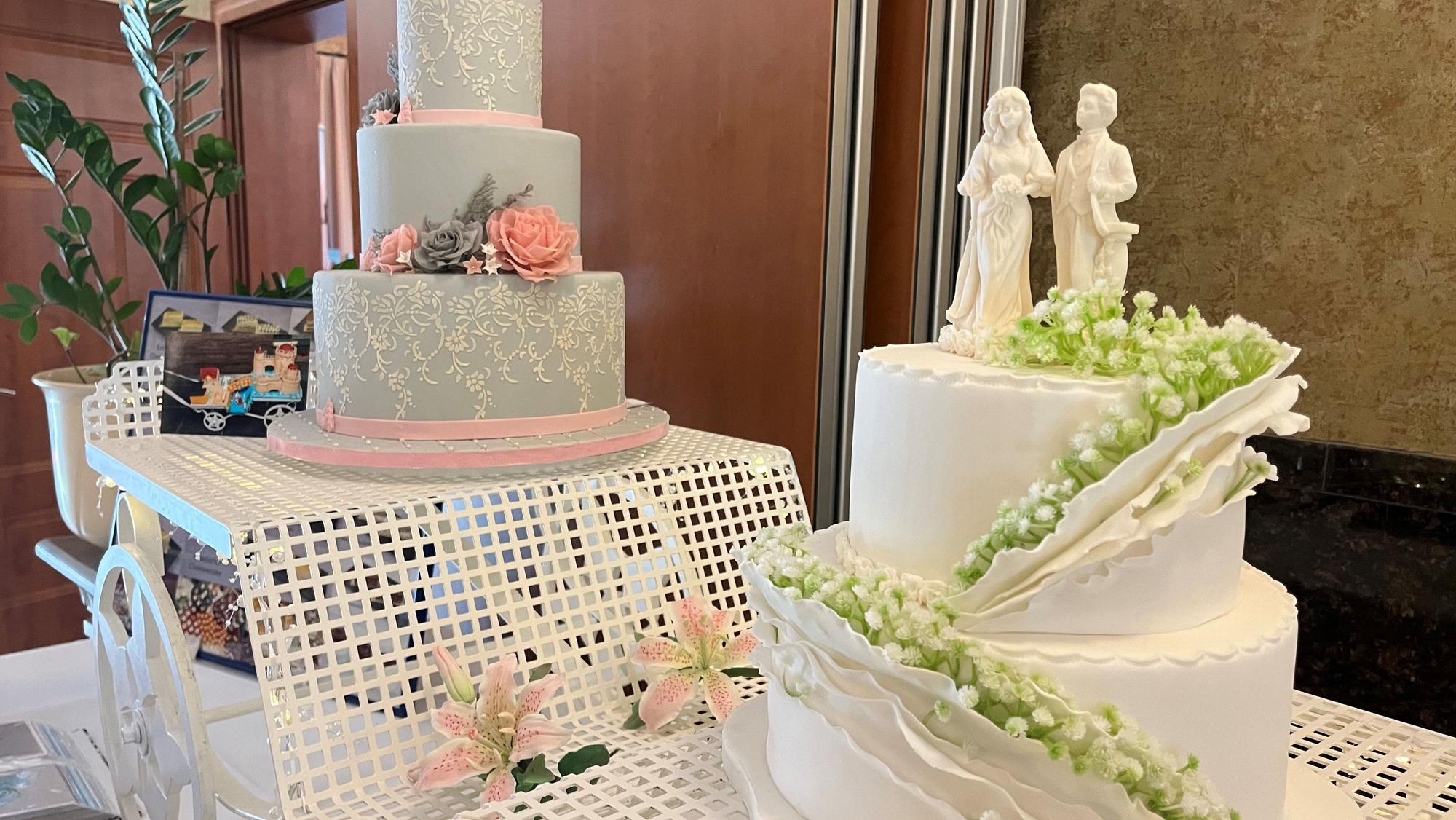Zwei mehrstöckige Hochzeitstorten mitstilisiertem Paar on top.