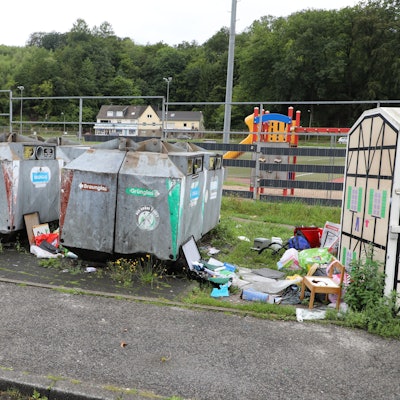 Neben Sammelcontainern liegt allerhand Müll auf dem Boden.