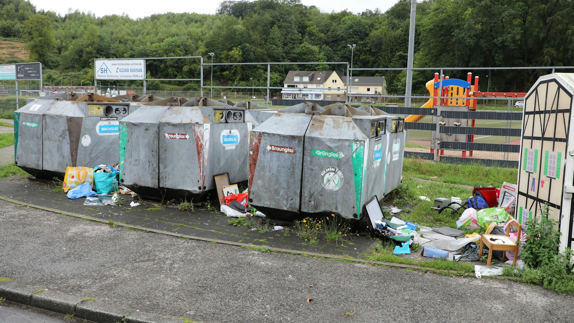 Neben Sammelcontainern liegt allerhand Müll auf dem Boden.
