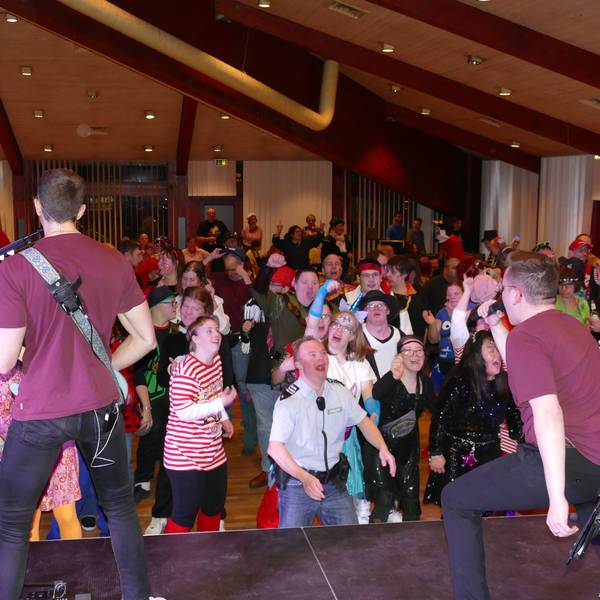 Eine Band spielt auf der Bühne, davor tanzen kostümierte Menschen.