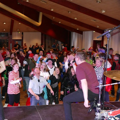 Eine Band spielt auf der Bühne, davor tanzen kostümierte Menschen.