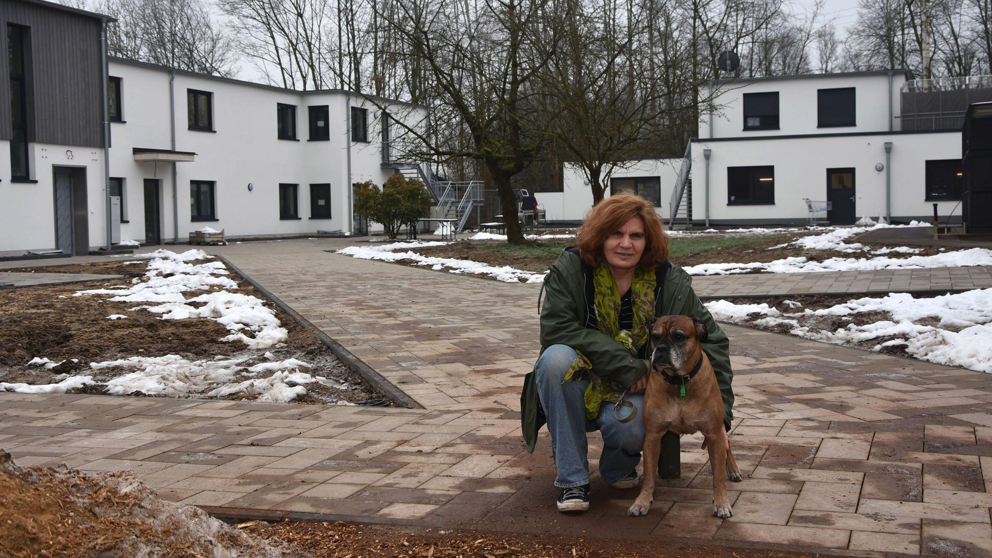 Zu sehen ist eine Frau mit einem alten Boxerhund vor neuen Gebäuden.
