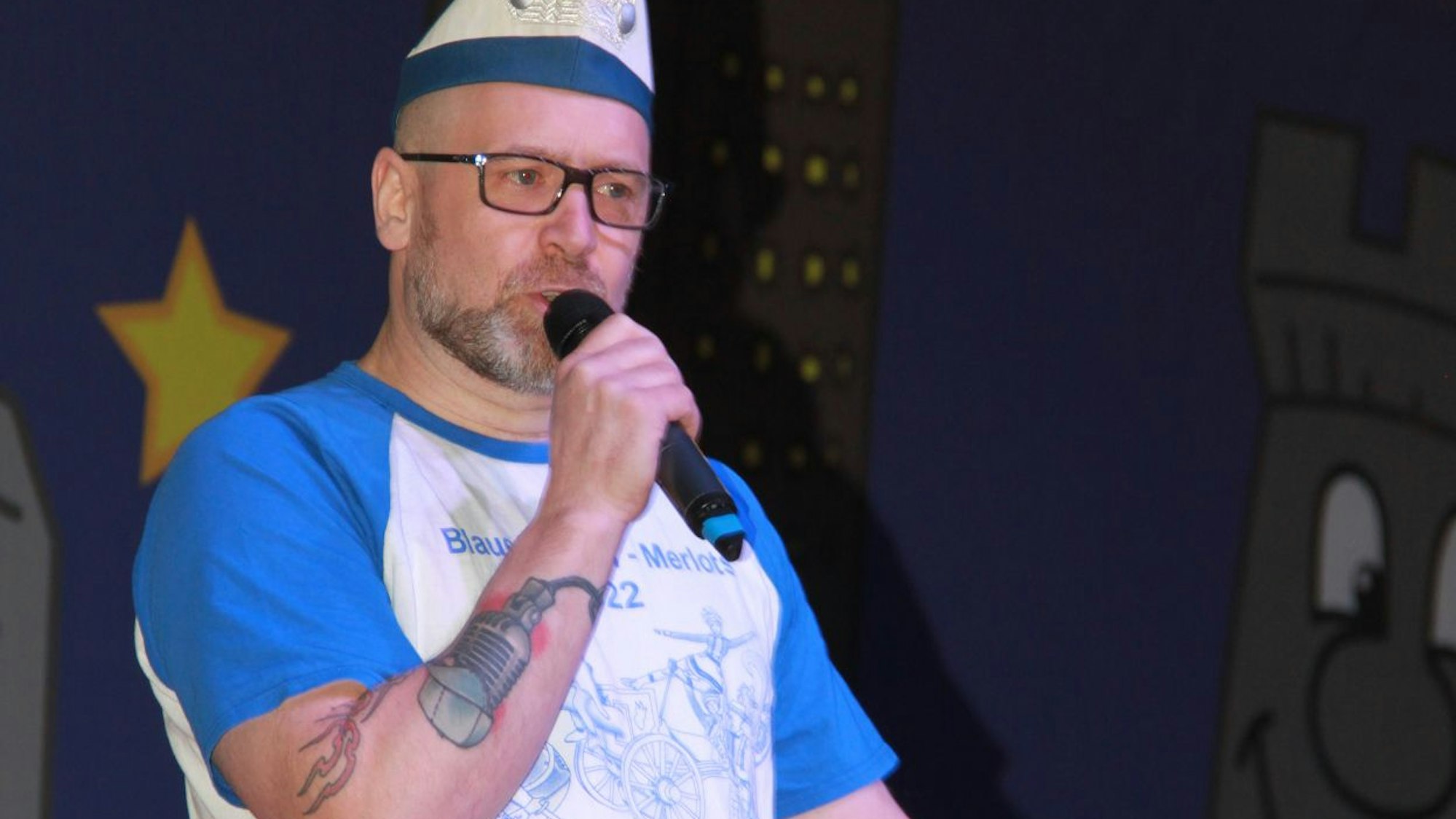 Das Bild zeigt Jens Bongard auf der Bühne mit einem Mikrofon in der Hand.