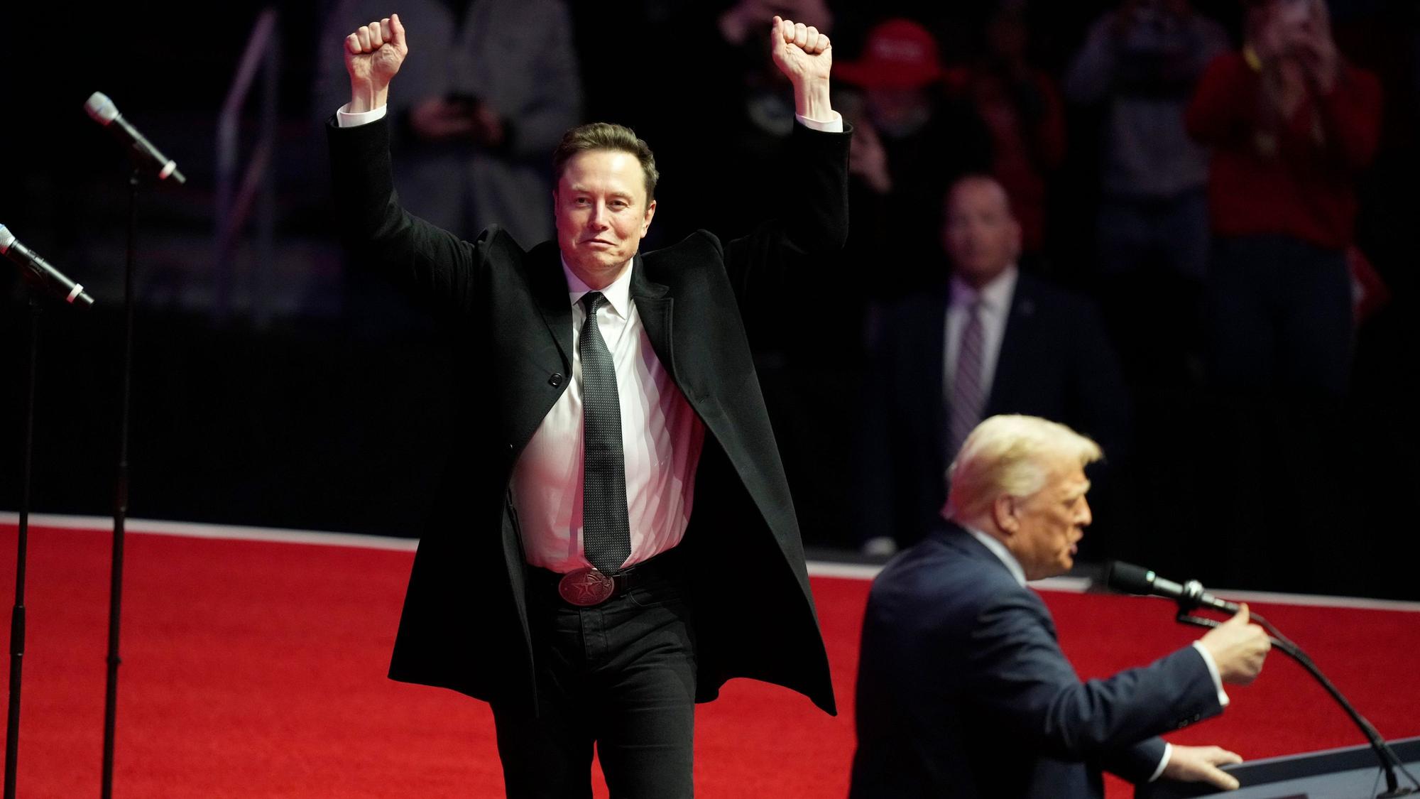 Elon Musk in Siegerpose, während der designierte US-Präsident Donald Trump auf einer Kundgebung vor seiner Amtseinführung spricht.