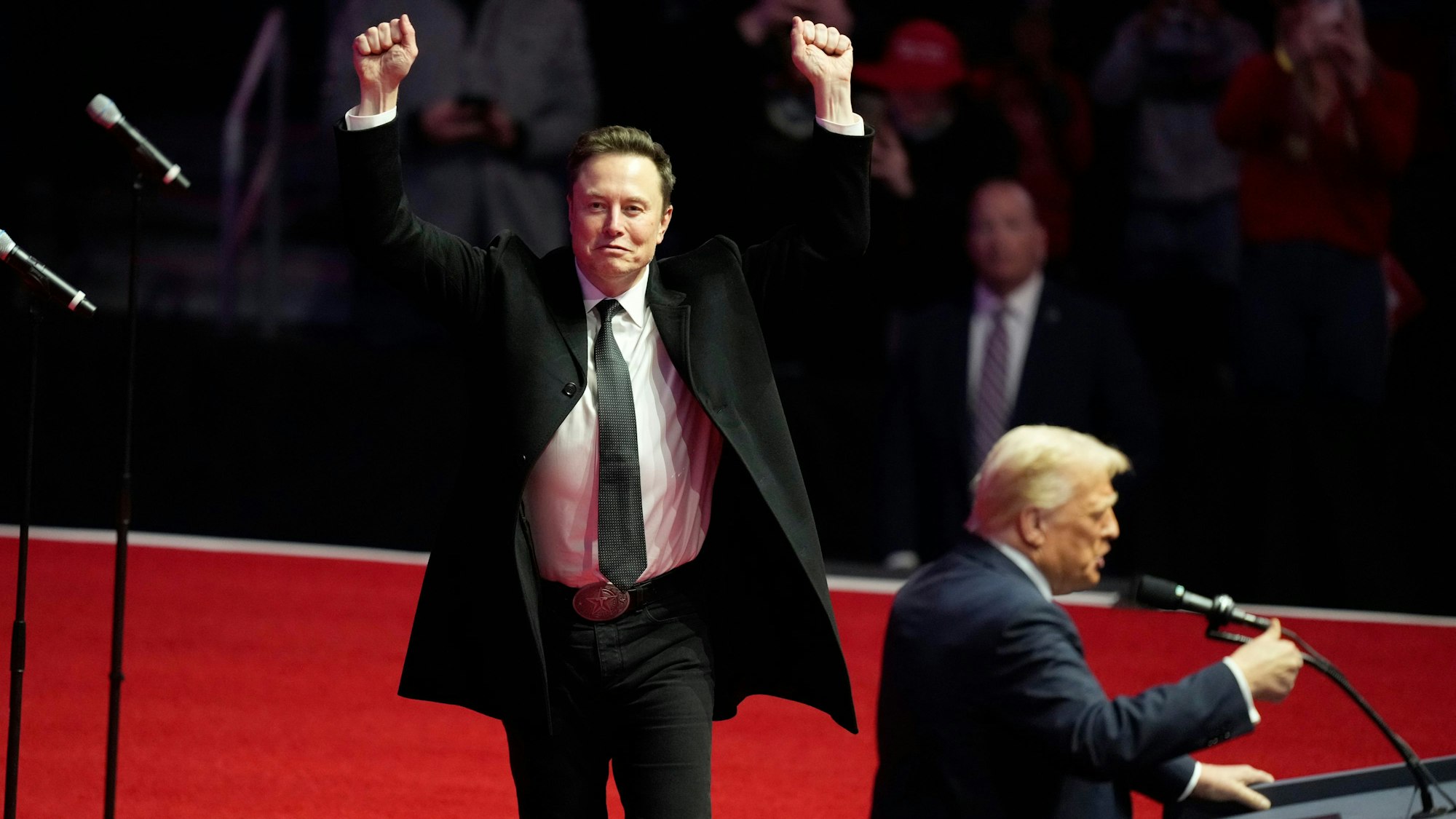 Elon Musk in Siegerpose, während der designierte US-Präsident Donald Trump auf einer Kundgebung vor seiner Amtseinführung spricht.