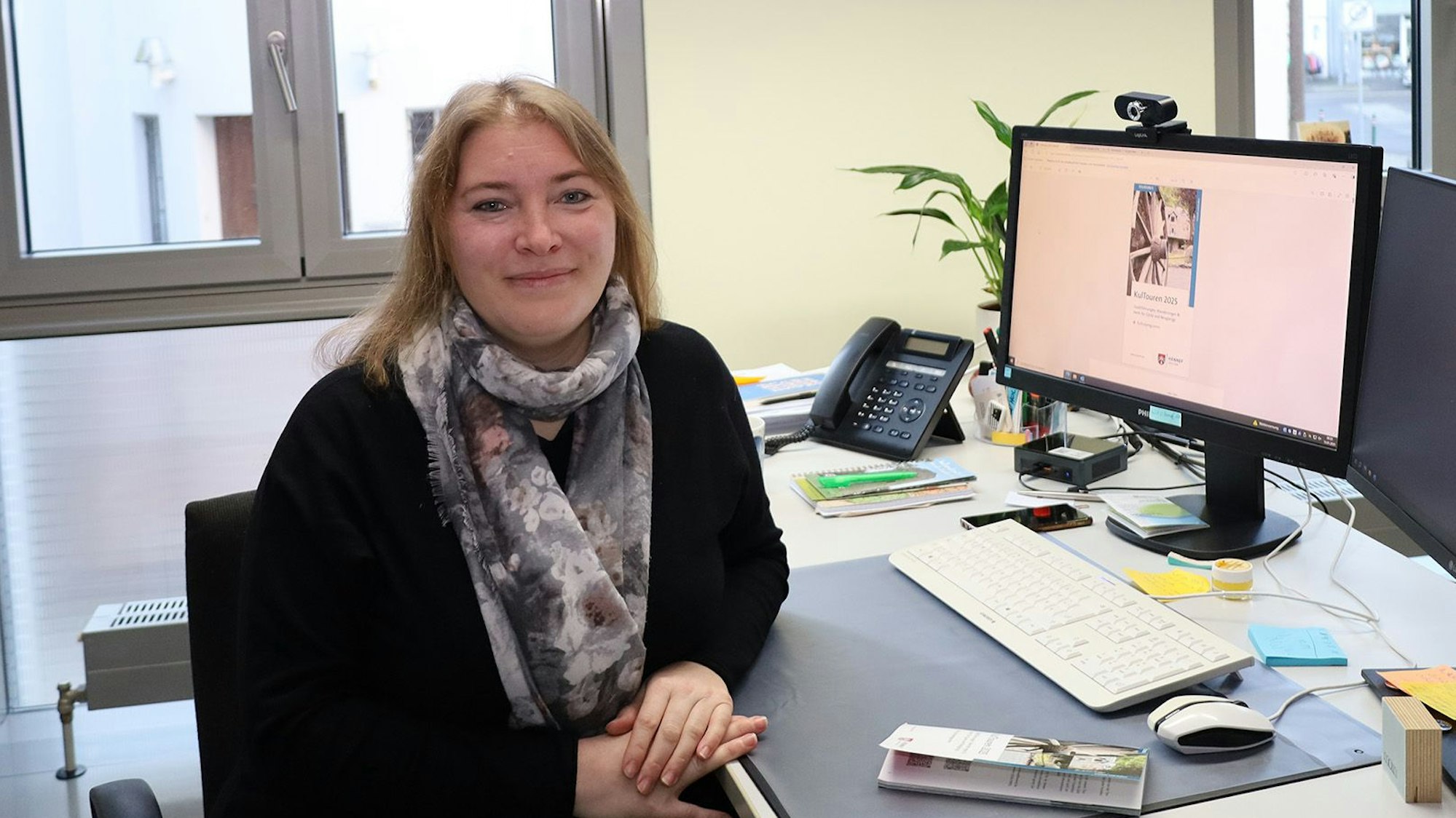 Eine Frau in einem Büro mit Schreibtisch und Computer-Monitor.
