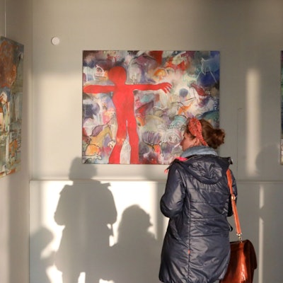 Eine Frau betrachtet großformatige Bilder, die sehr bunt sind.