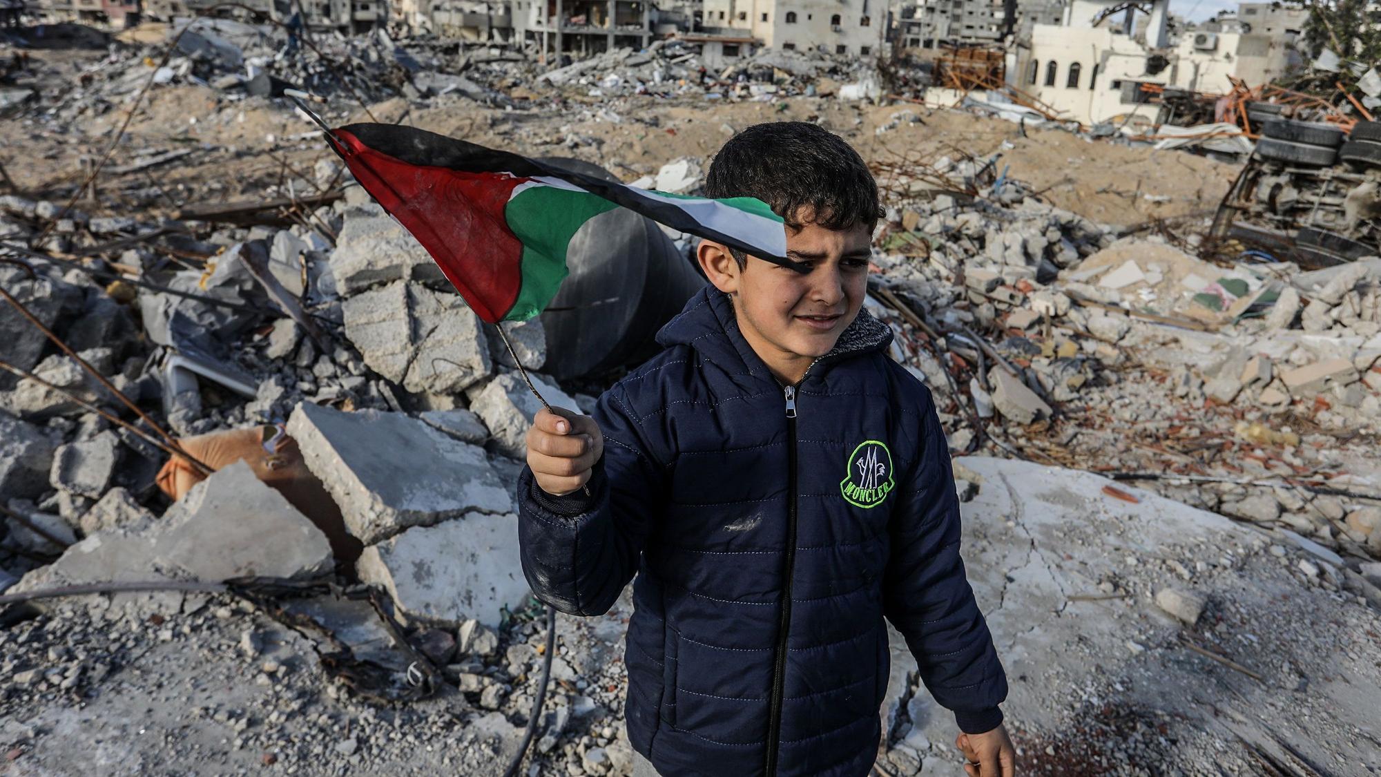 Ein vertriebener palästinensischer Junge, der eine Fahne schwenkt, steht auf Trümmern von Gebäuden, einen Tag nach Inkrafttreten eines Abkommens über eine Waffenruhe zwischen Israel und der Hamas im Gazastreifen.