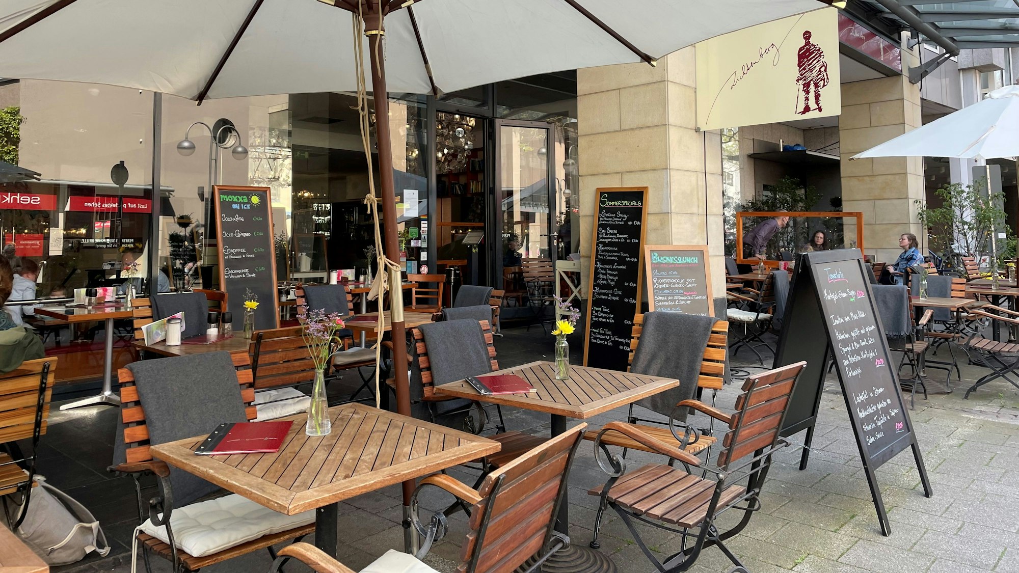 Das Cafe Lichtenberg: Stühle, Tische, ein Schirm. Ein Schild mit der Aufschrift „Lichtenberg“.