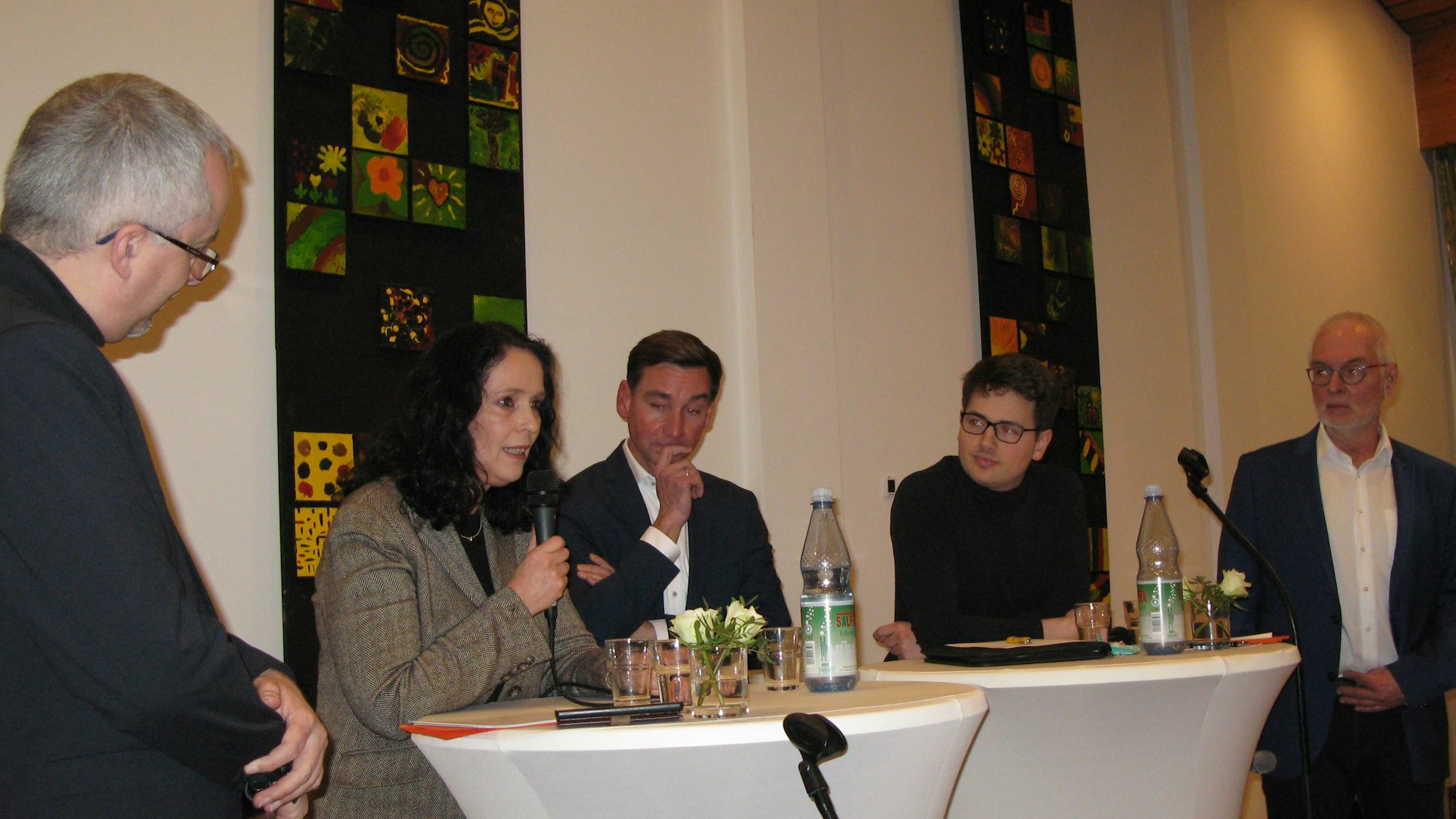 Eine Frau und vier Männer an Stehtischen auf einem Podium.