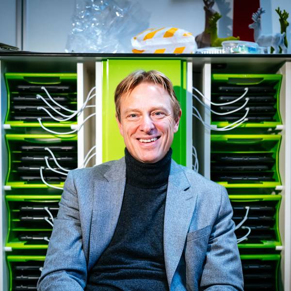 Schulleiter Andre Szymkowiak sitzt vor einem Regal, in dem iPads laden.