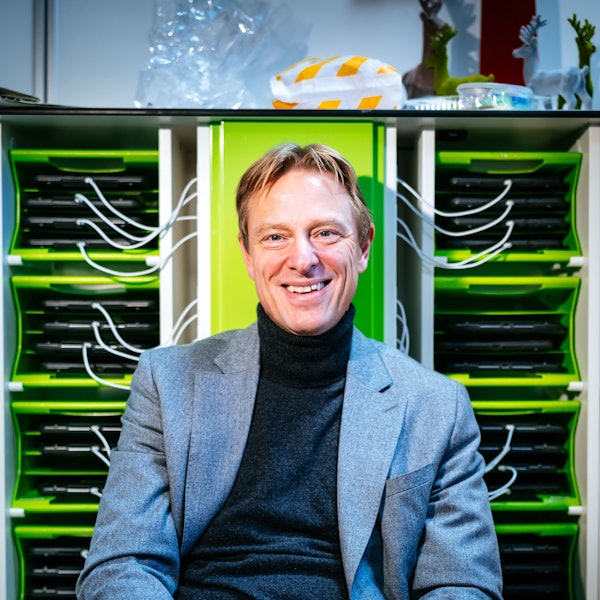 Schulleiter Andre Szymkowiak sitzt vor einem Regal, in dem iPads laden.