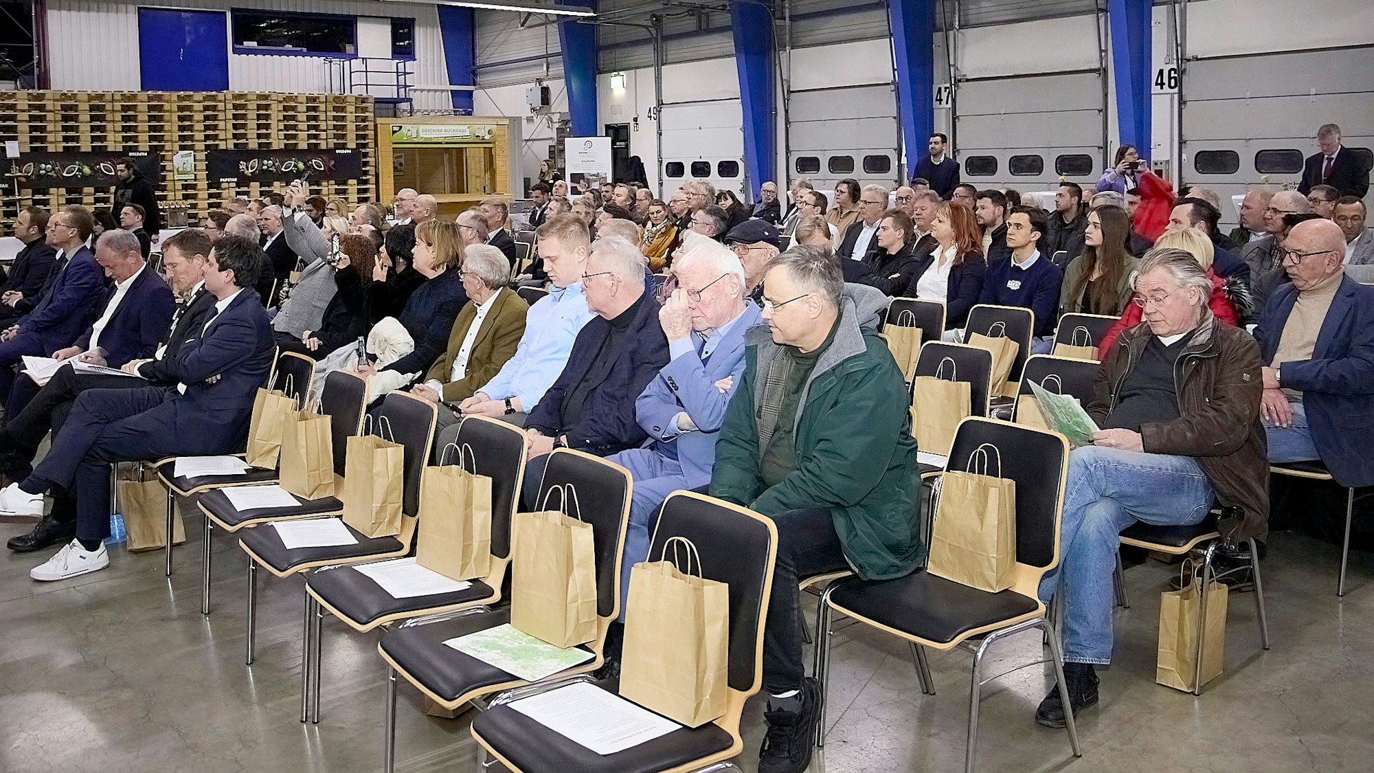 Zahlreiche Menschen sitzen auf Stühlen in einer Halle im Logistikzentrum von Papstar in Kall.