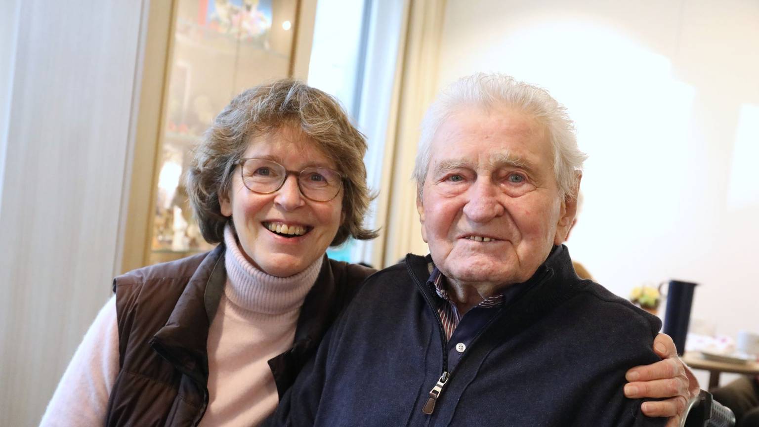 Eine Frau und ein Mann sitzen nebeneinander, sie hat einen Arm um ihn gelegt.