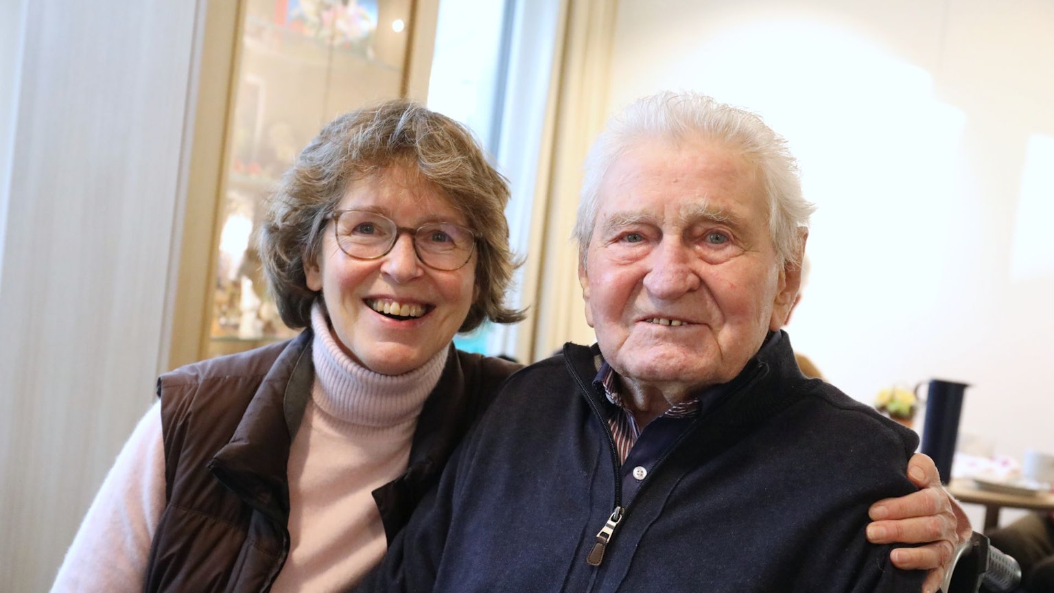 Eine Frau und ein Mann sitzen nebeneinander, sie hat einen Arm um ihn gelegt.