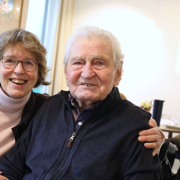 Eine Frau und ein Mann sitzen nebeneinander, sie hat einen Arm um ihn gelegt.