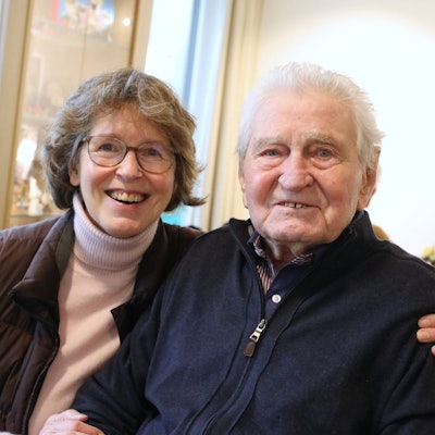 Eine Frau und ein Mann sitzen nebeneinander, sie hat einen Arm um ihn gelegt.